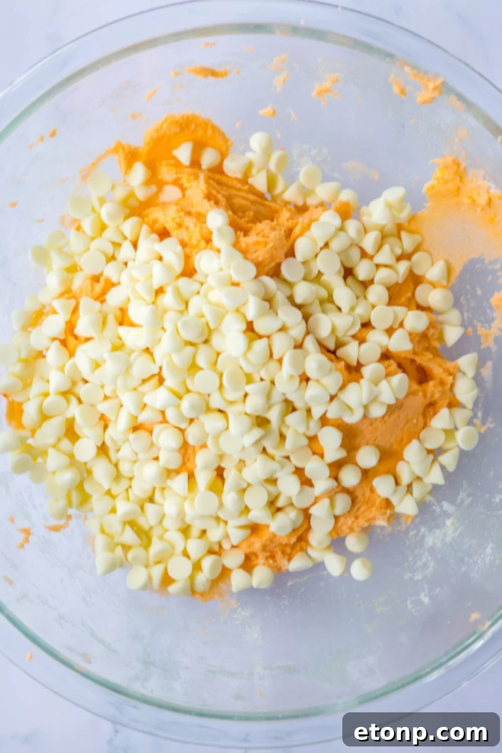white chocolate chips on top of a orange cookie batter in bowl 