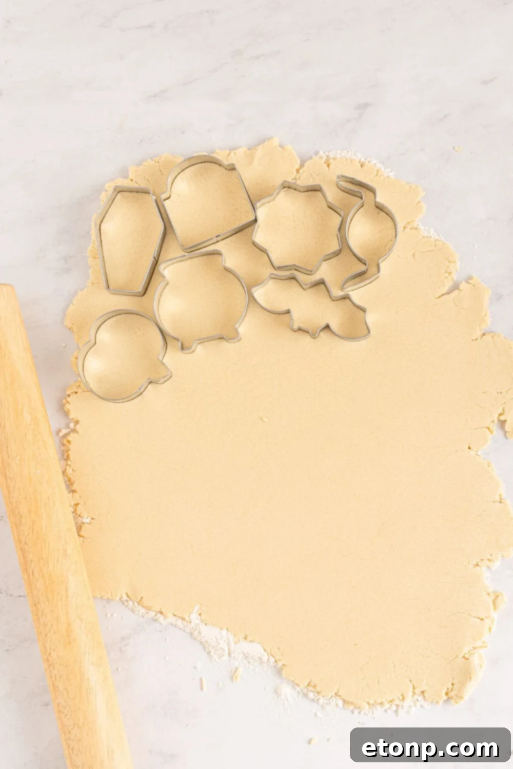 cookie cutters on sugar cookie dough as it is rolled out on table 