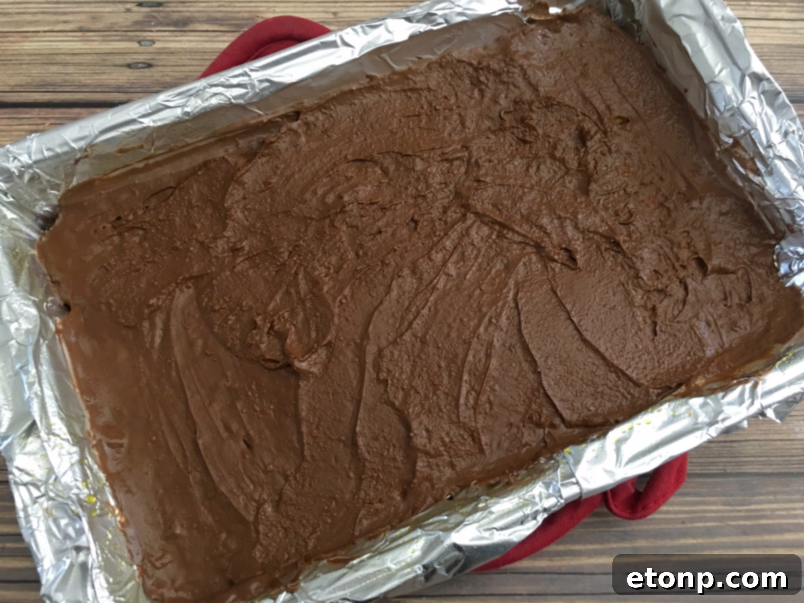 Melted chocolate being smoothly spread across the surface of the toffee-coated crackers