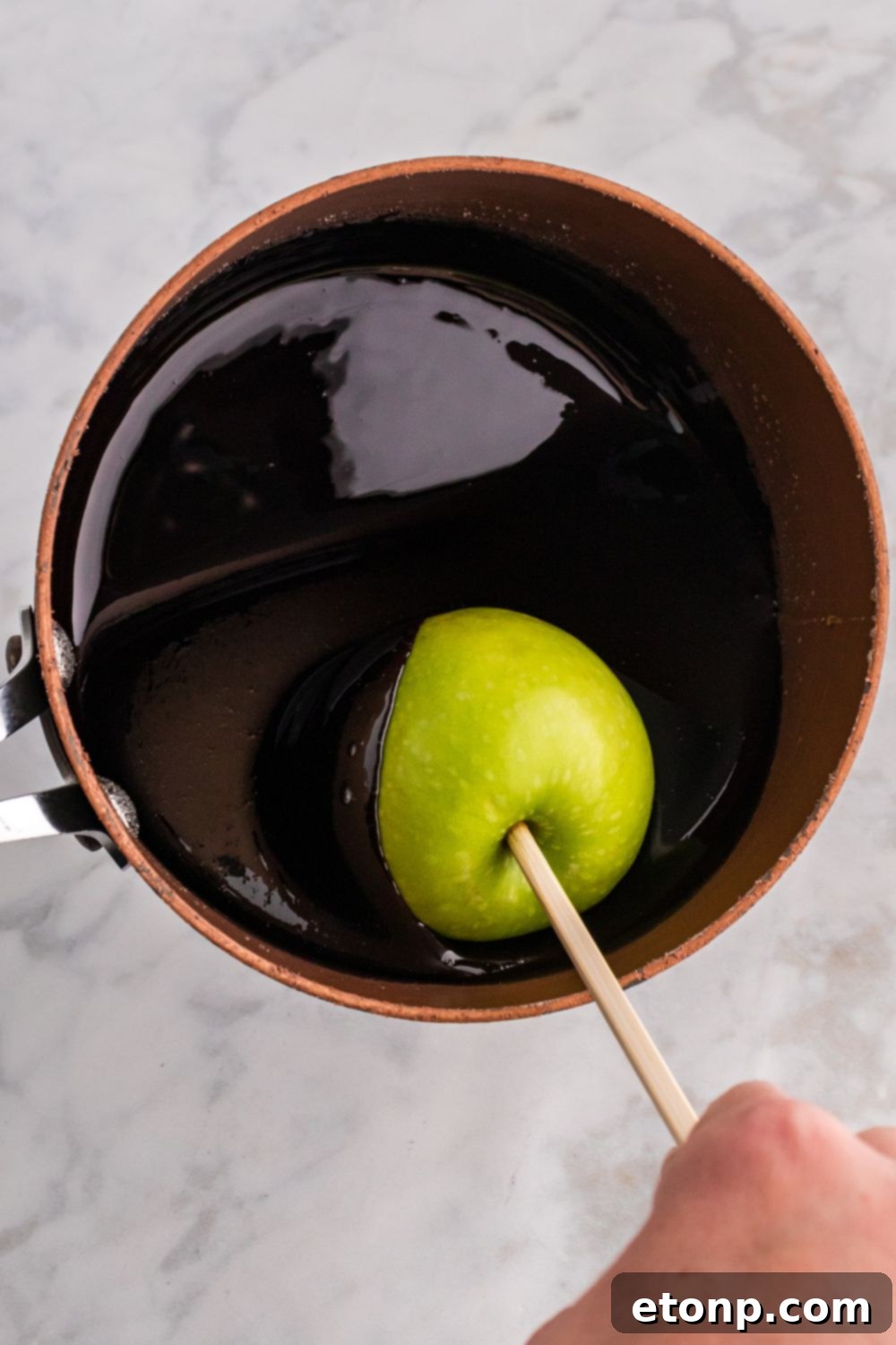 dipping apple on stick in a black candy coating 