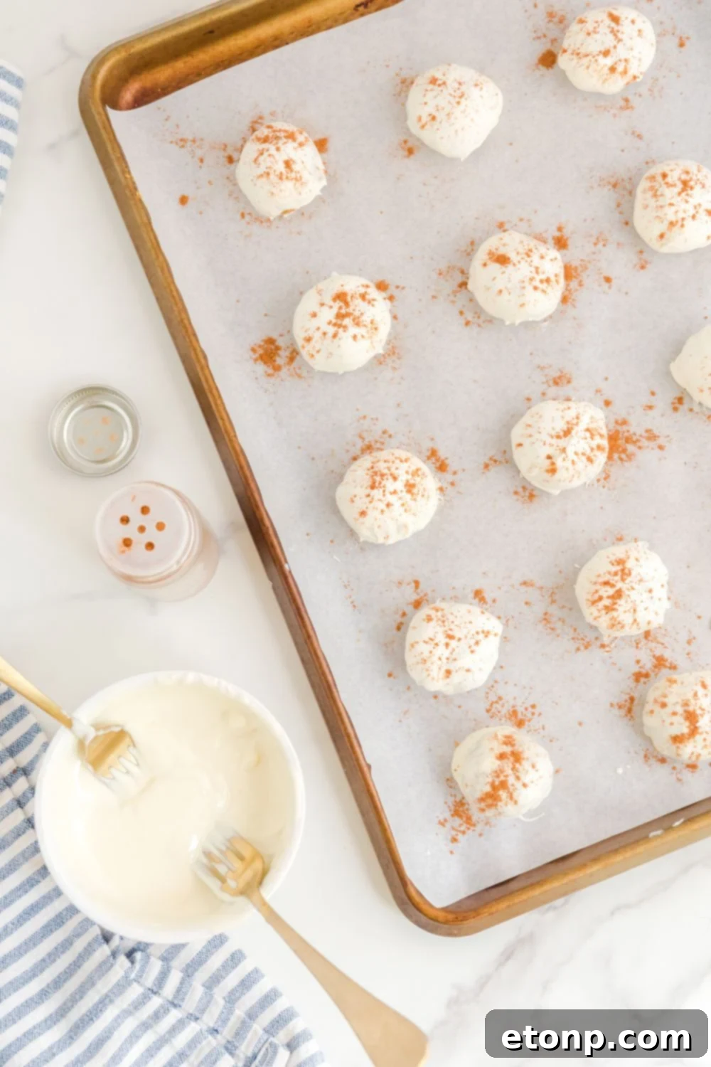 Finished Pumpkin Spice Cheesecake Bites artfully arranged on a baking sheet, with a bowl of melted chocolate ready for dipping nearby.