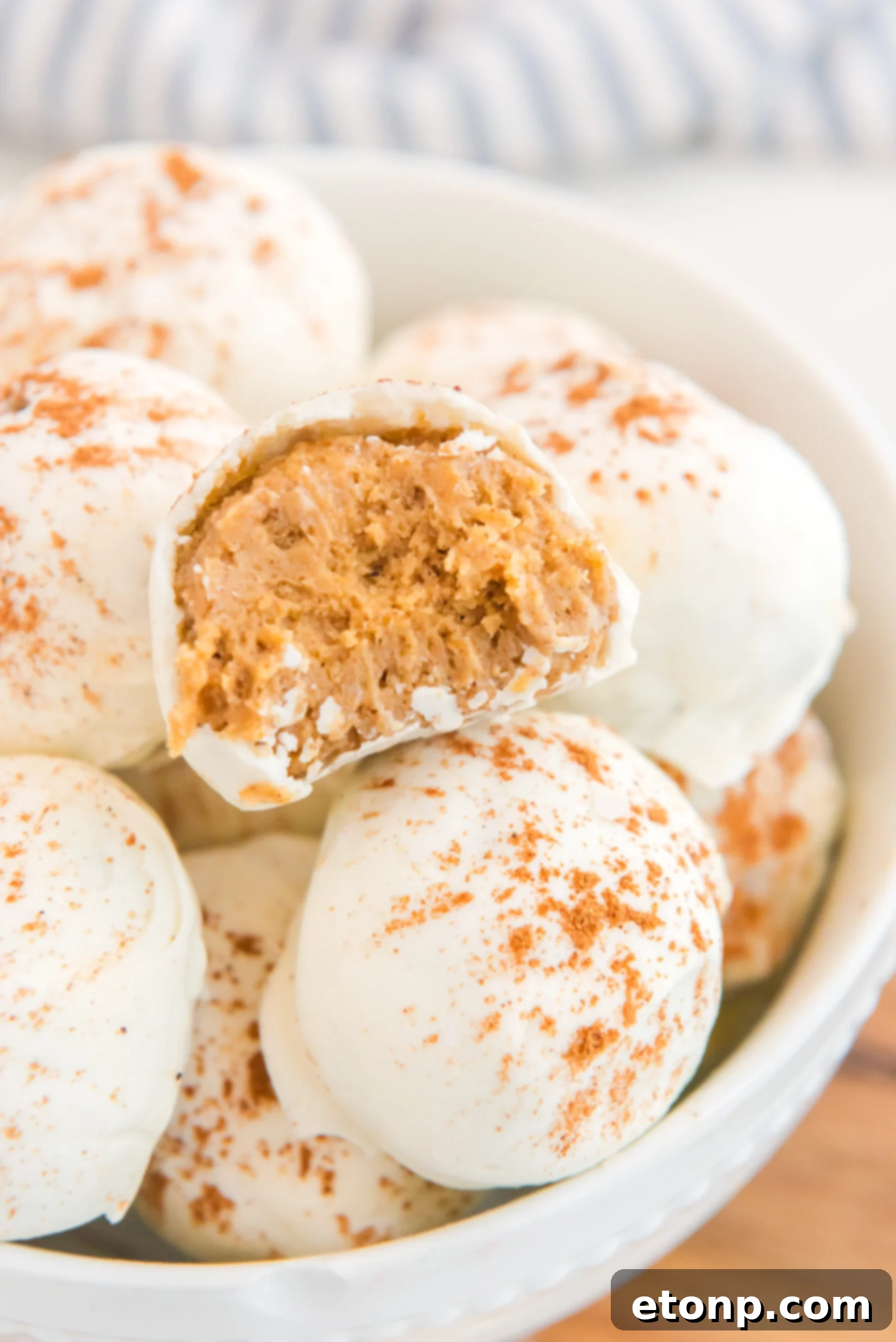 A stack of no-bake pumpkin balls in a bowl, with one bite taken out, showing the delectable filling.