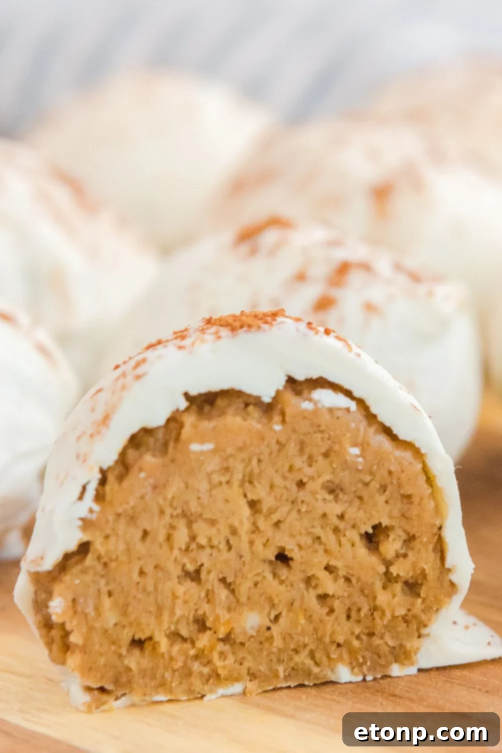 A single pumpkin spice ball, elegantly cut in half, presented on a wooden board to highlight its smooth interior.