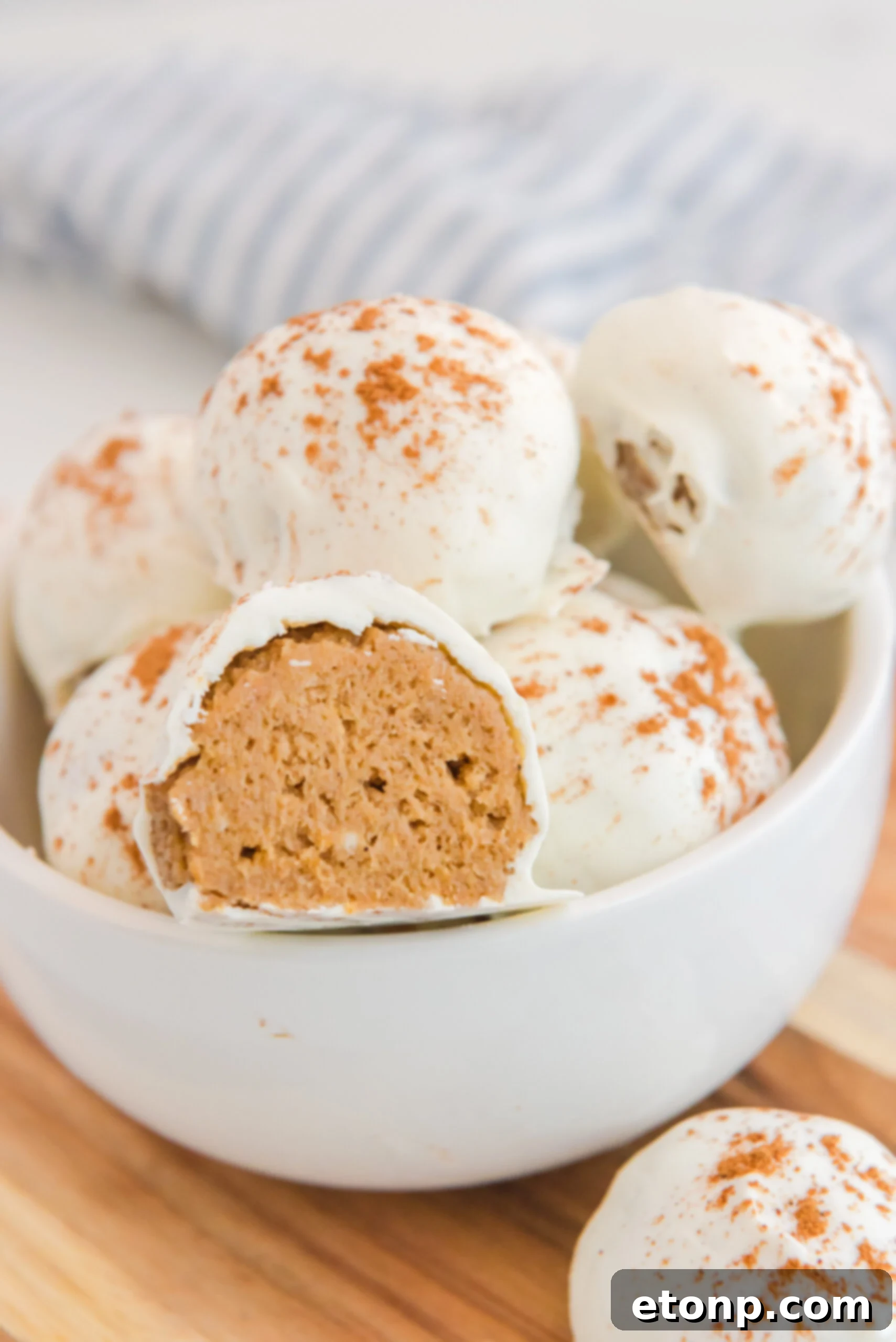A bowl of no-bake pumpkin balls, with one piece cut open to display its moist and inviting texture.