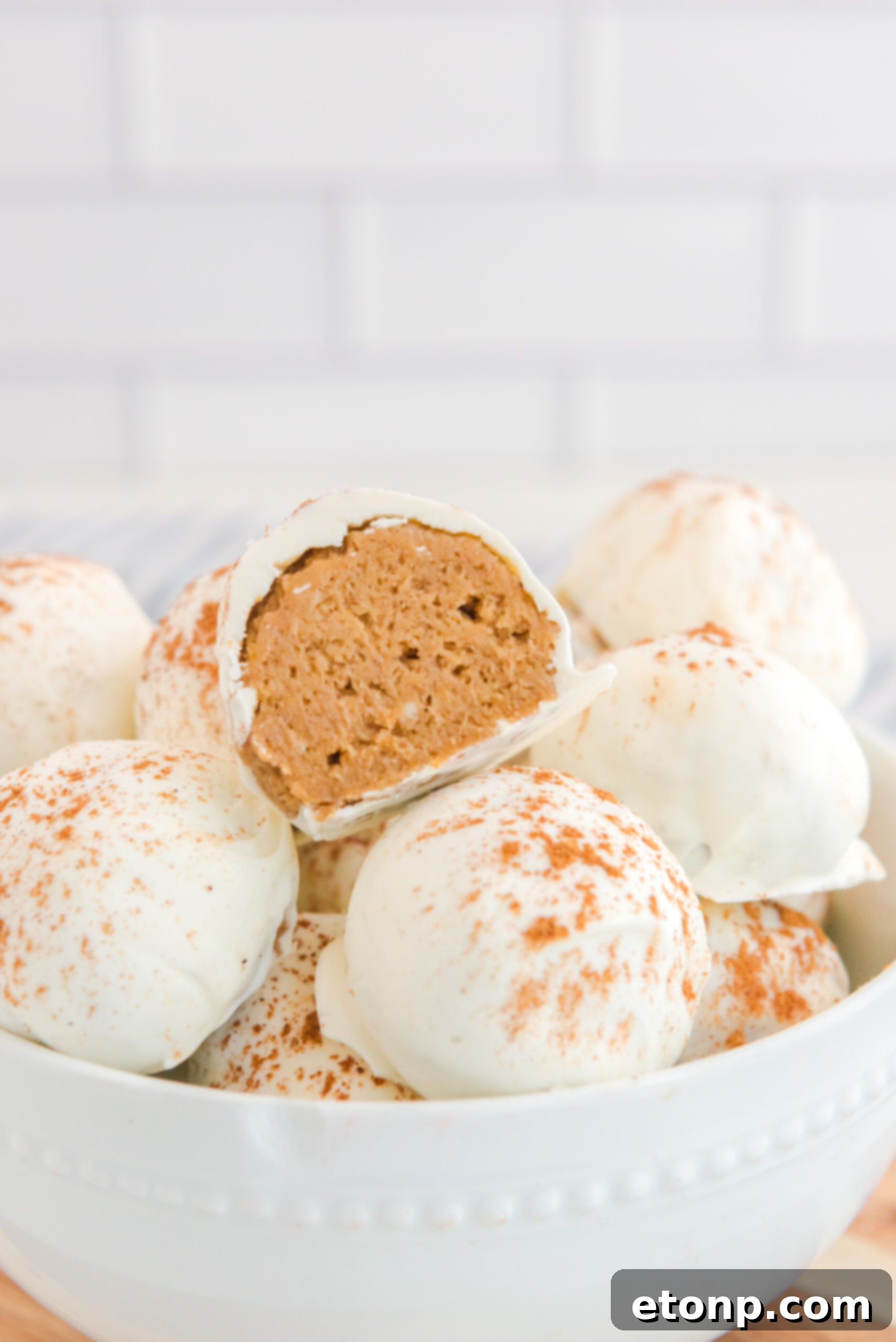 Close-up of no-bake pumpkin balls in a white bowl, with one cut open to show the smooth, inviting interior texture.