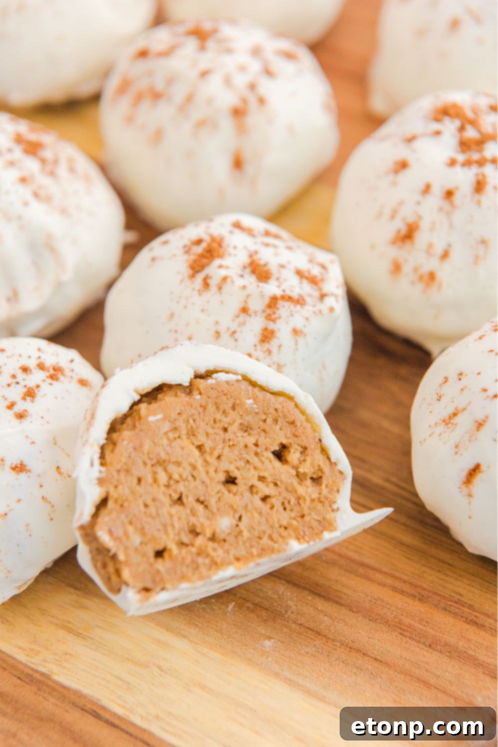 A collection of perfectly formed cheesecake balls with pumpkin flavor, arranged on a table, with one piece expertly sliced in half to showcase its creamy interior.