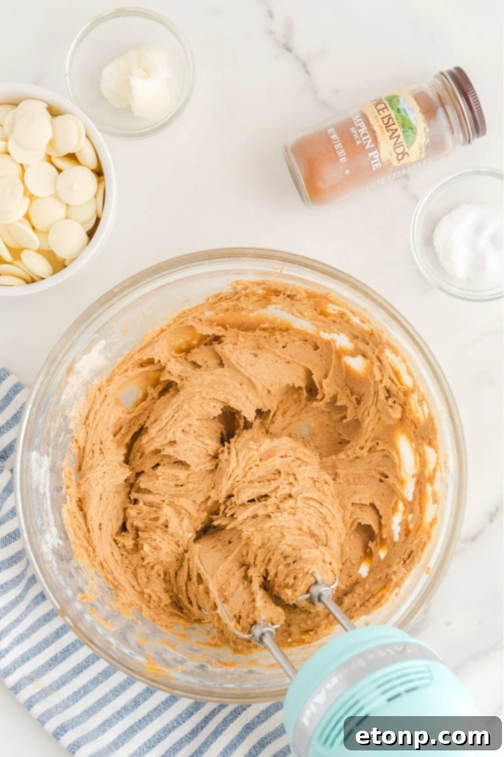 The pumpkin cheesecake mixture being expertly blended with a hand mixer in a large glass bowl, creating a smooth batter.