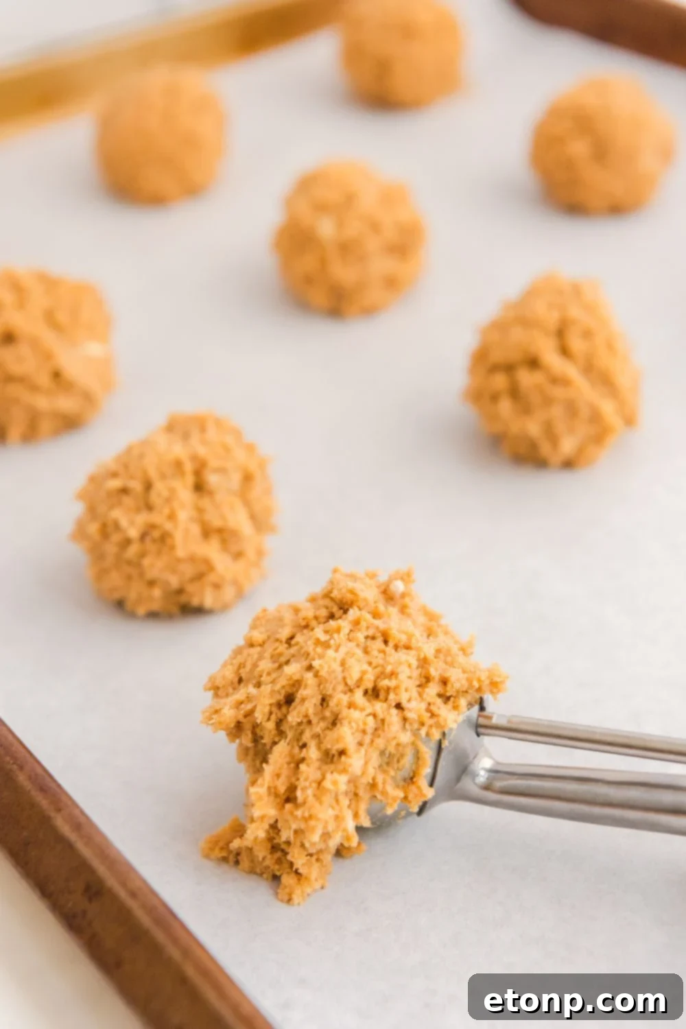 A cookie scoop holding a portion of the prepared cheesecake batter, showing its consistency before rolling.