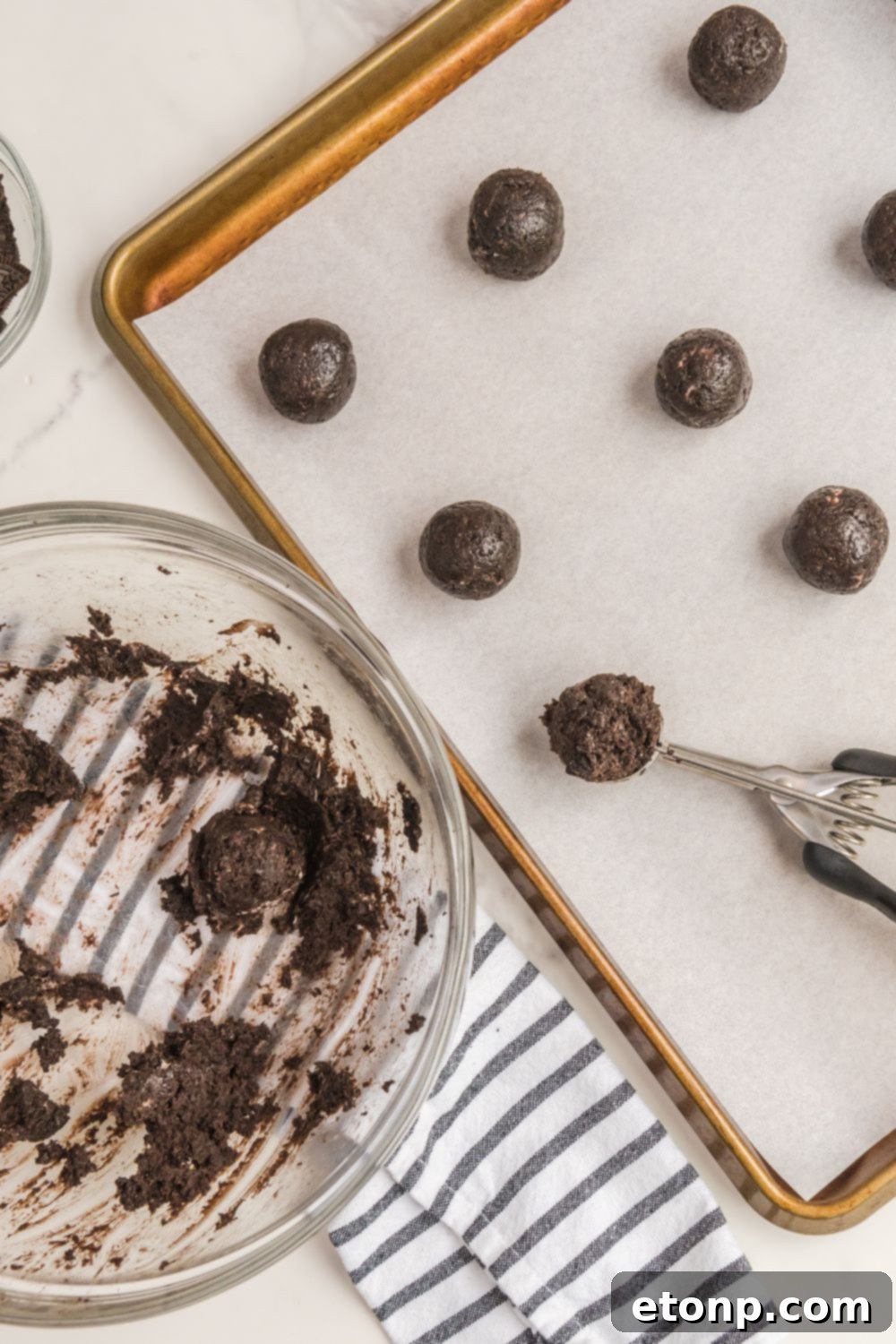 Neatly rolled Oreo balls placed on a parchment-lined cookie sheet, chilling