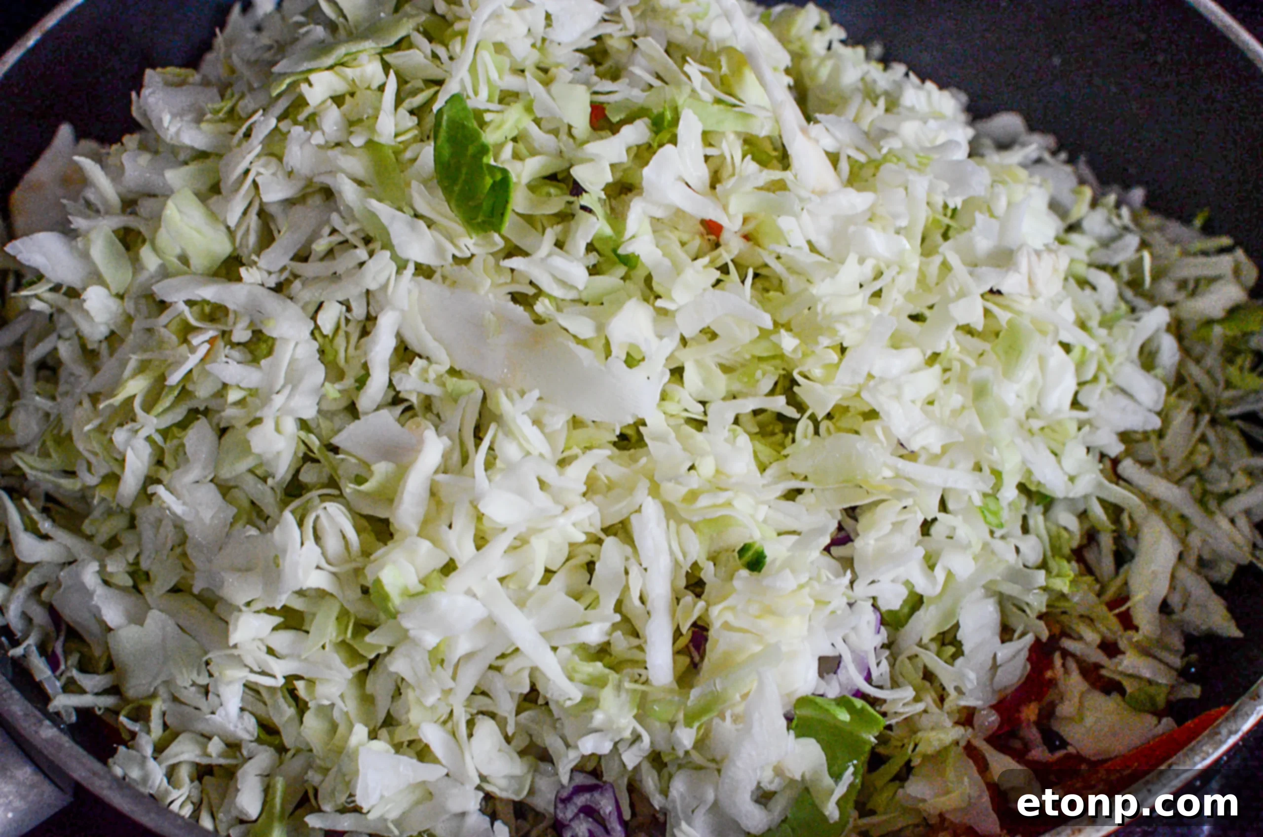 Shredded cabbage added to the beef and vegetable mixture in a wok