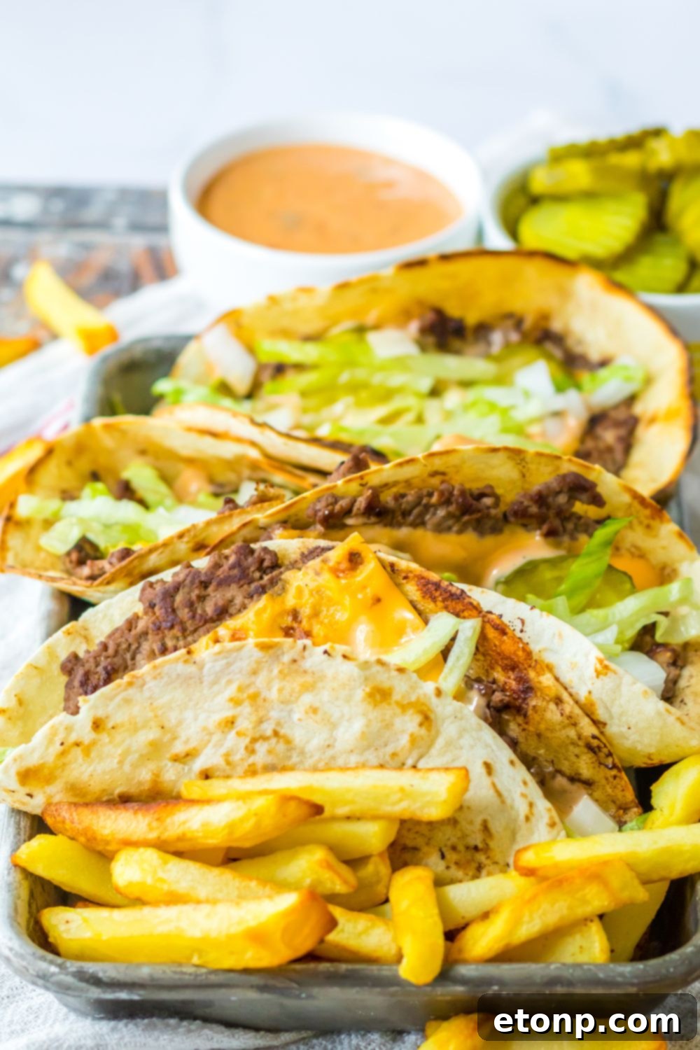 Fries and burger tacos on a table with condiments in containers behind it