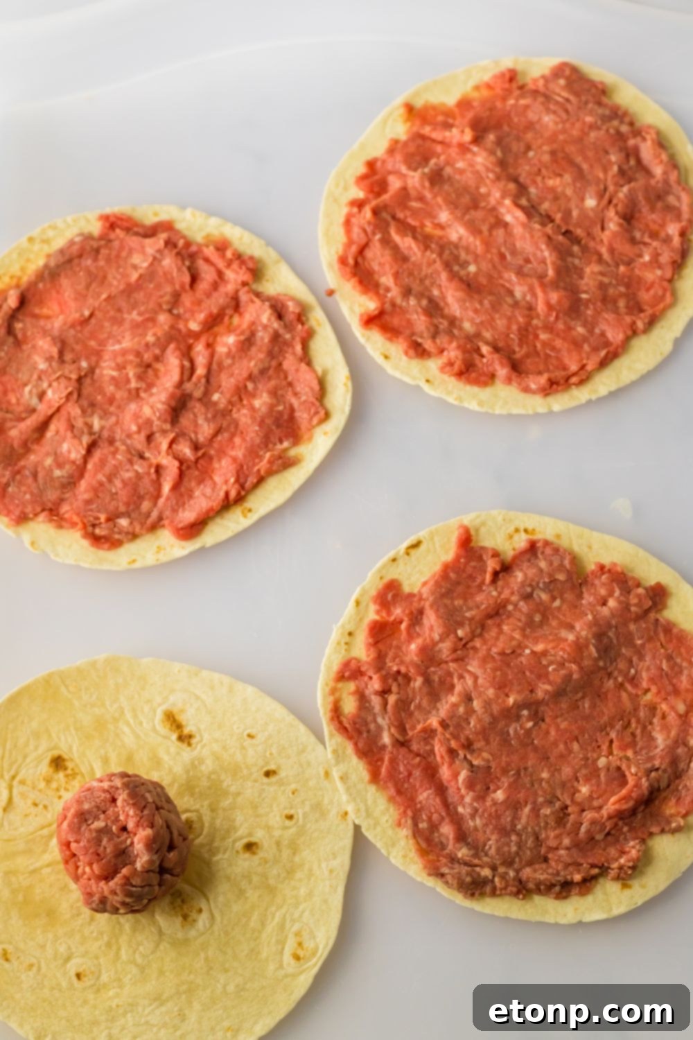 Flour tortilla with burger meat smashed on it, ready for cooking