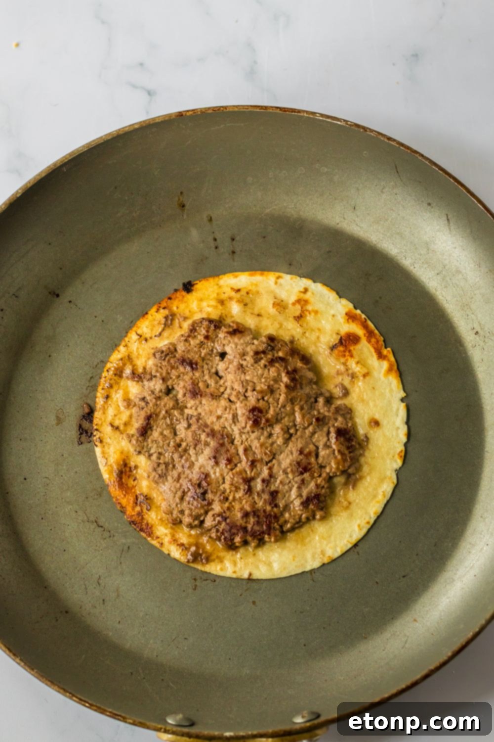 Crispy tortilla with a cooked burger patty on top