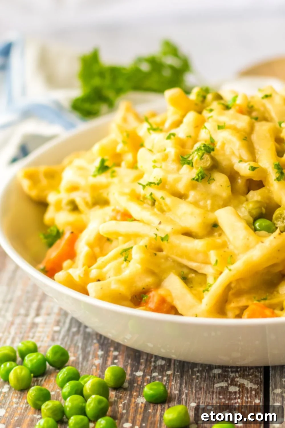 white bowl with chicken and noodles and peas spread out on table