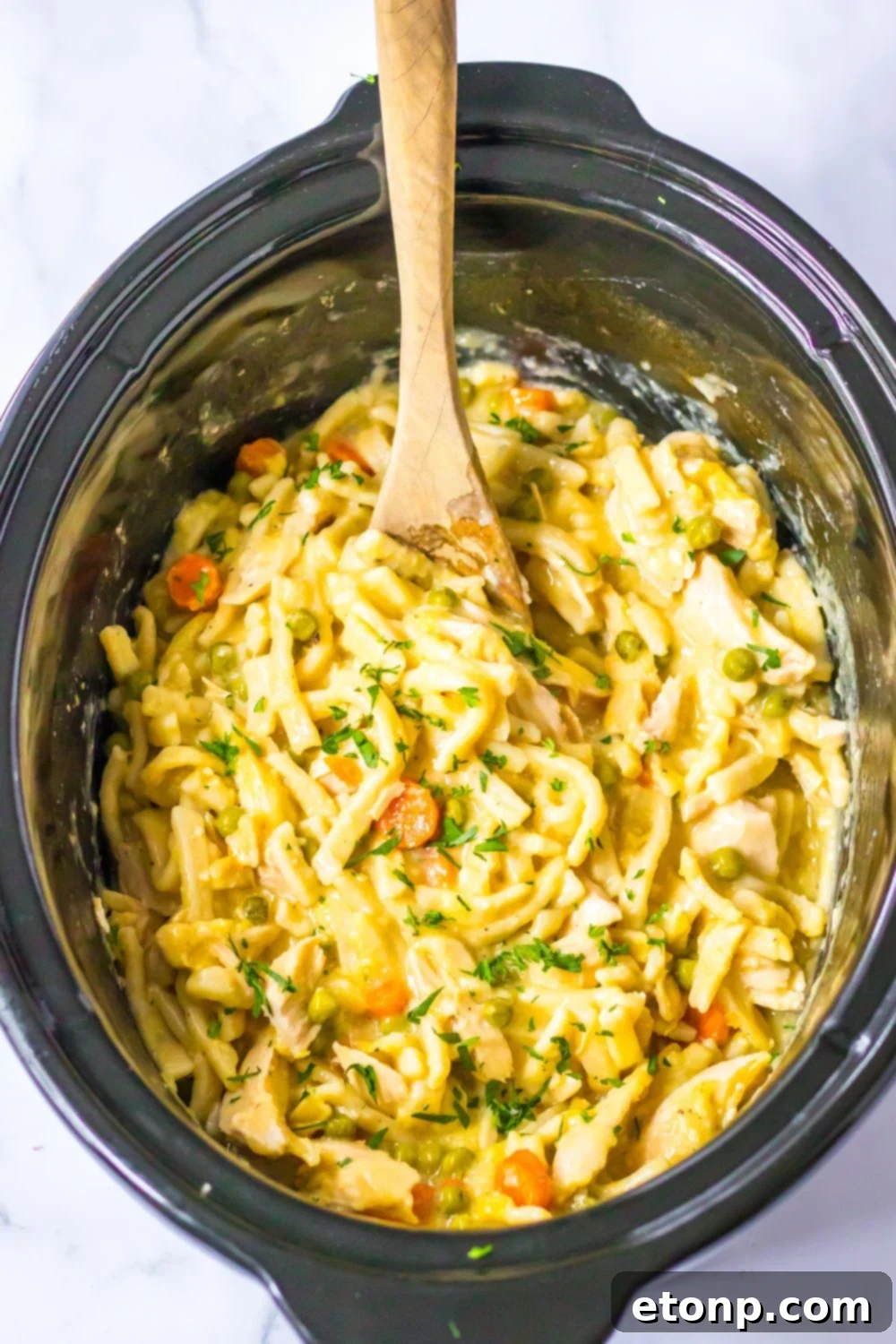 crockpot chicken noodle soup in a crockpot with a wooden spoon in it