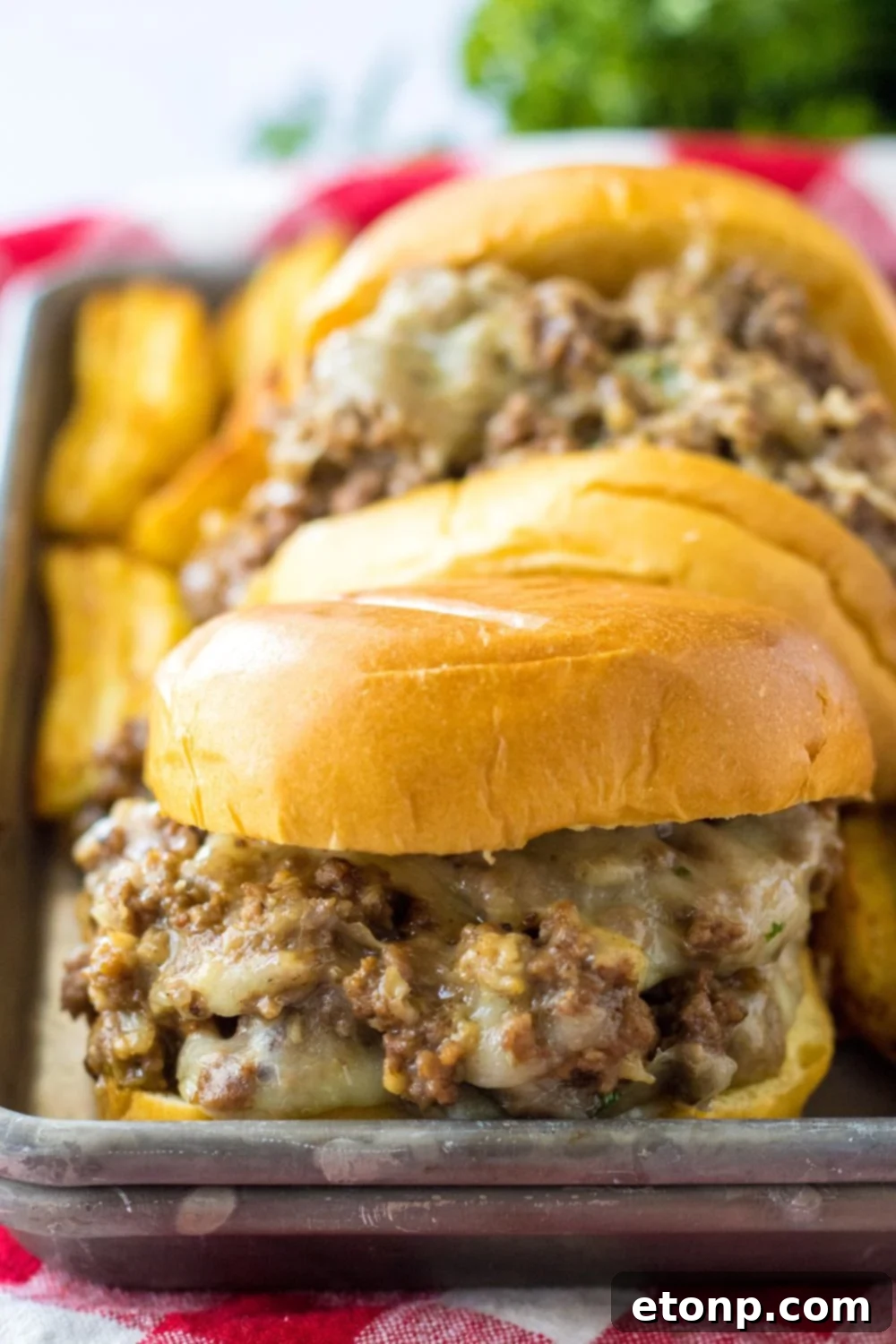 french dip sandwiches on a metal tray with potato wedges behind it 