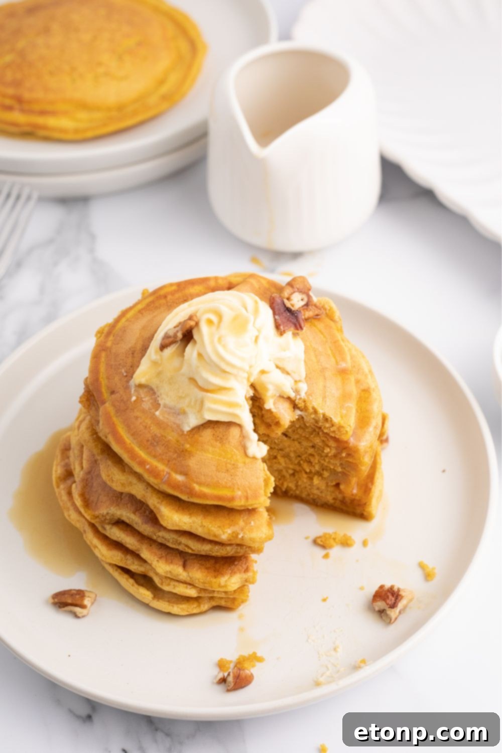 Pumpkin spice pancakes stacked on a plate, with some sliced, showcasing the fluffy interior