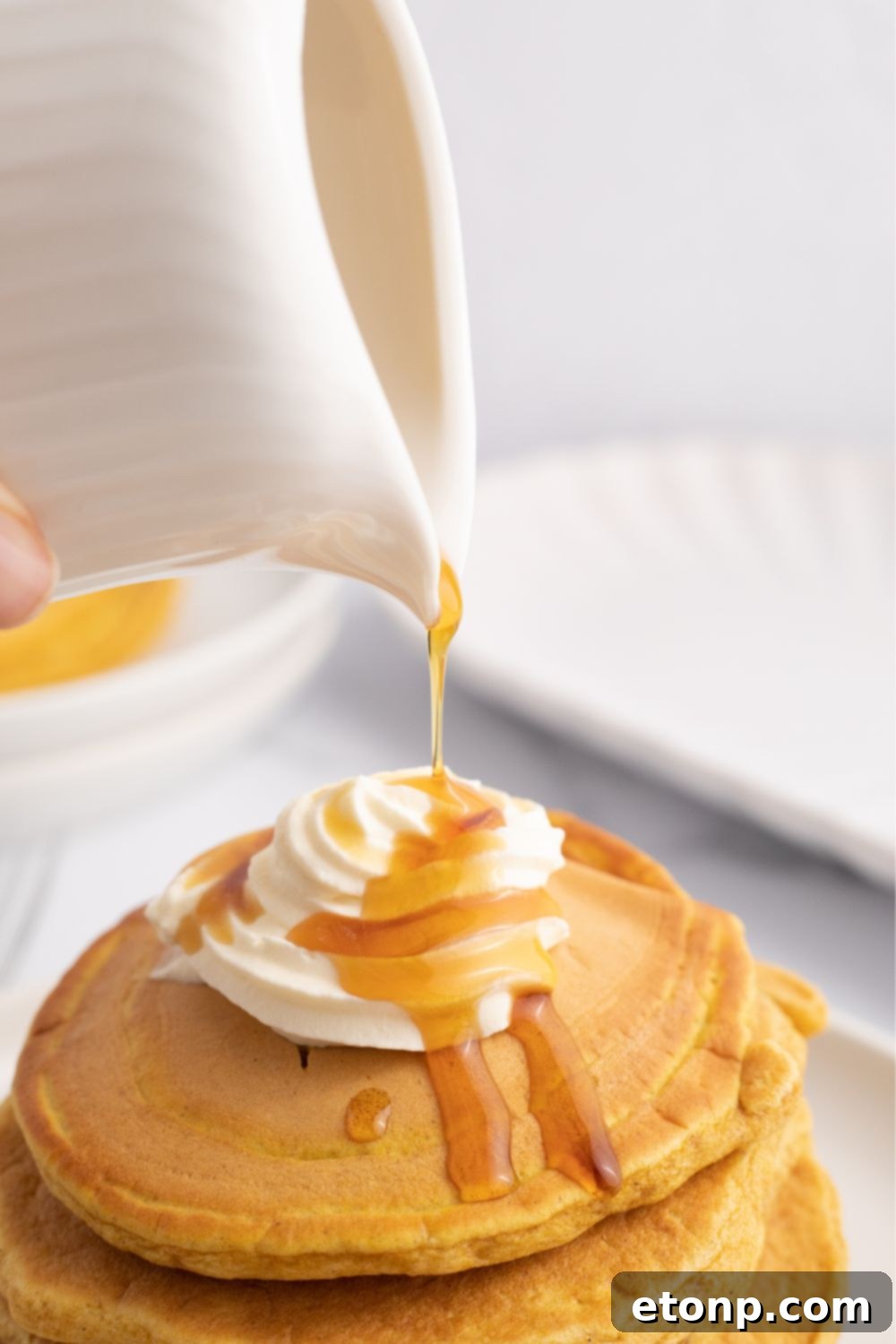 Maple syrup being poured generously over a stack of pumpkin pancakes