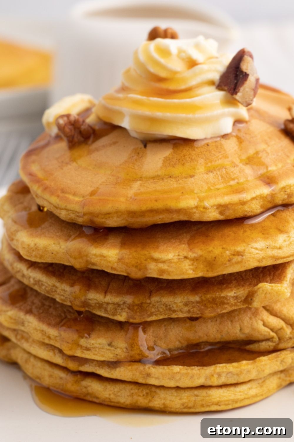 A stack of pumpkin pancakes topped with whipped cream and chopped nuts