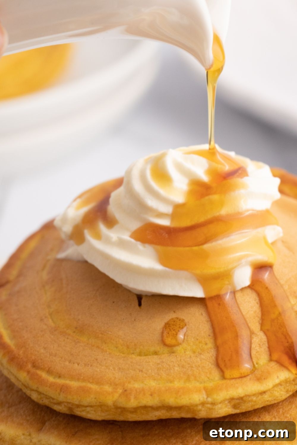 Syrup being drizzled artfully over a stack of golden pumpkin pancakes