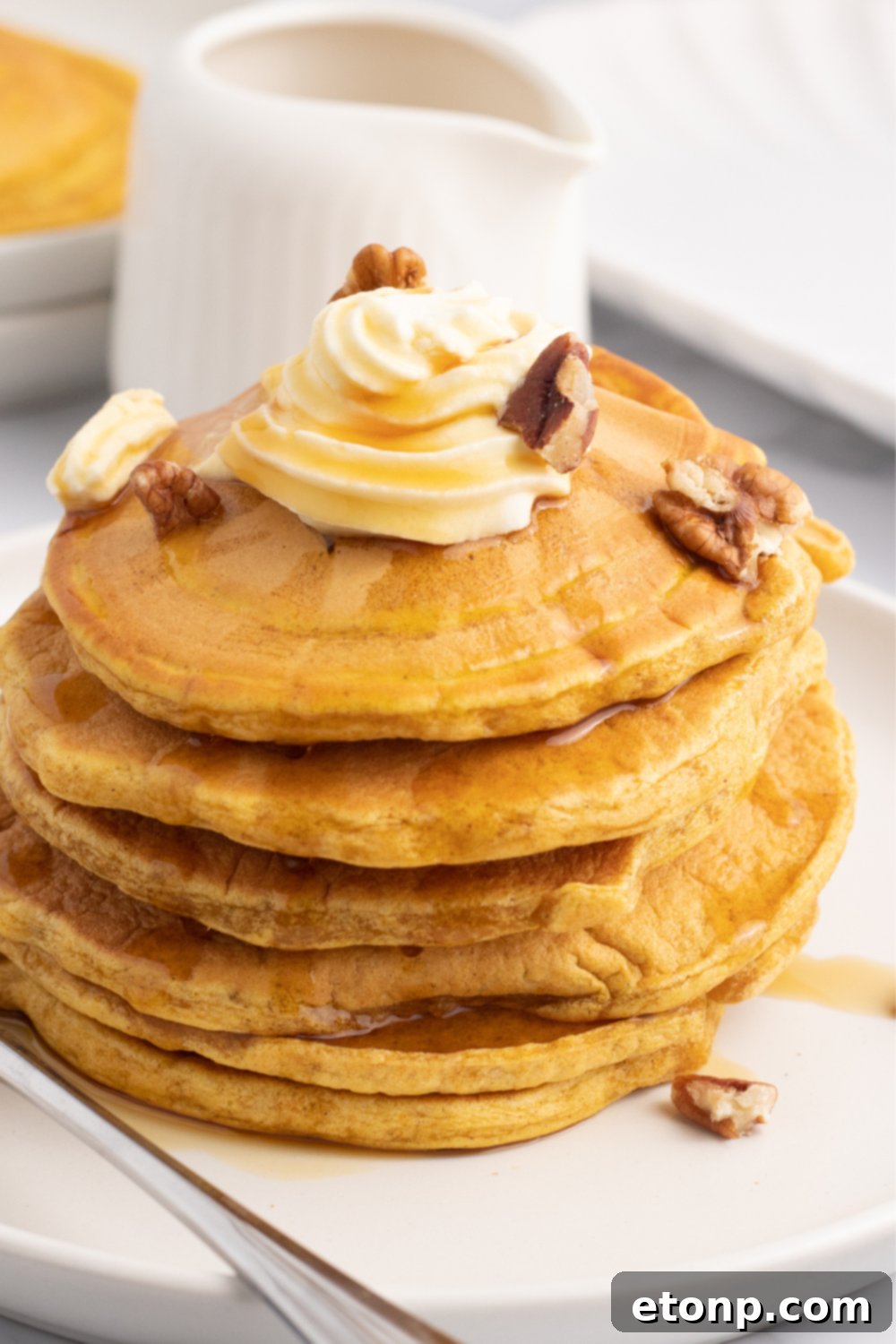 Stacked pumpkin pancakes on a plate with a bite taken out of the top one