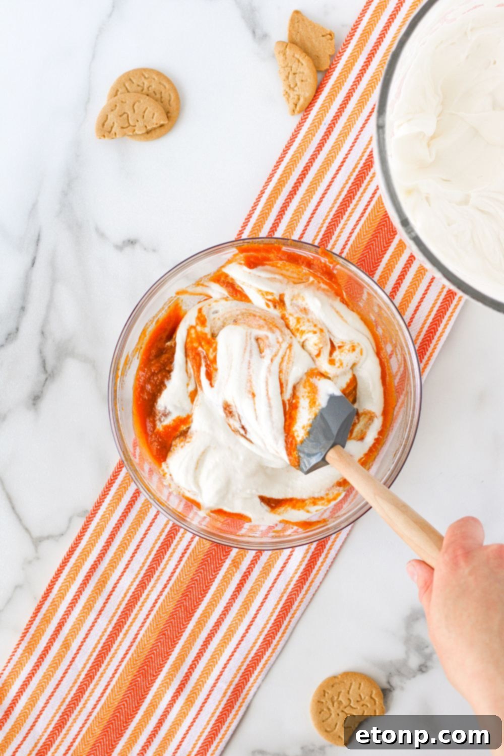 The process of gently mixing pumpkin puree into the whipped cream and condensed milk base, creating the flavorful pumpkin ice cream.