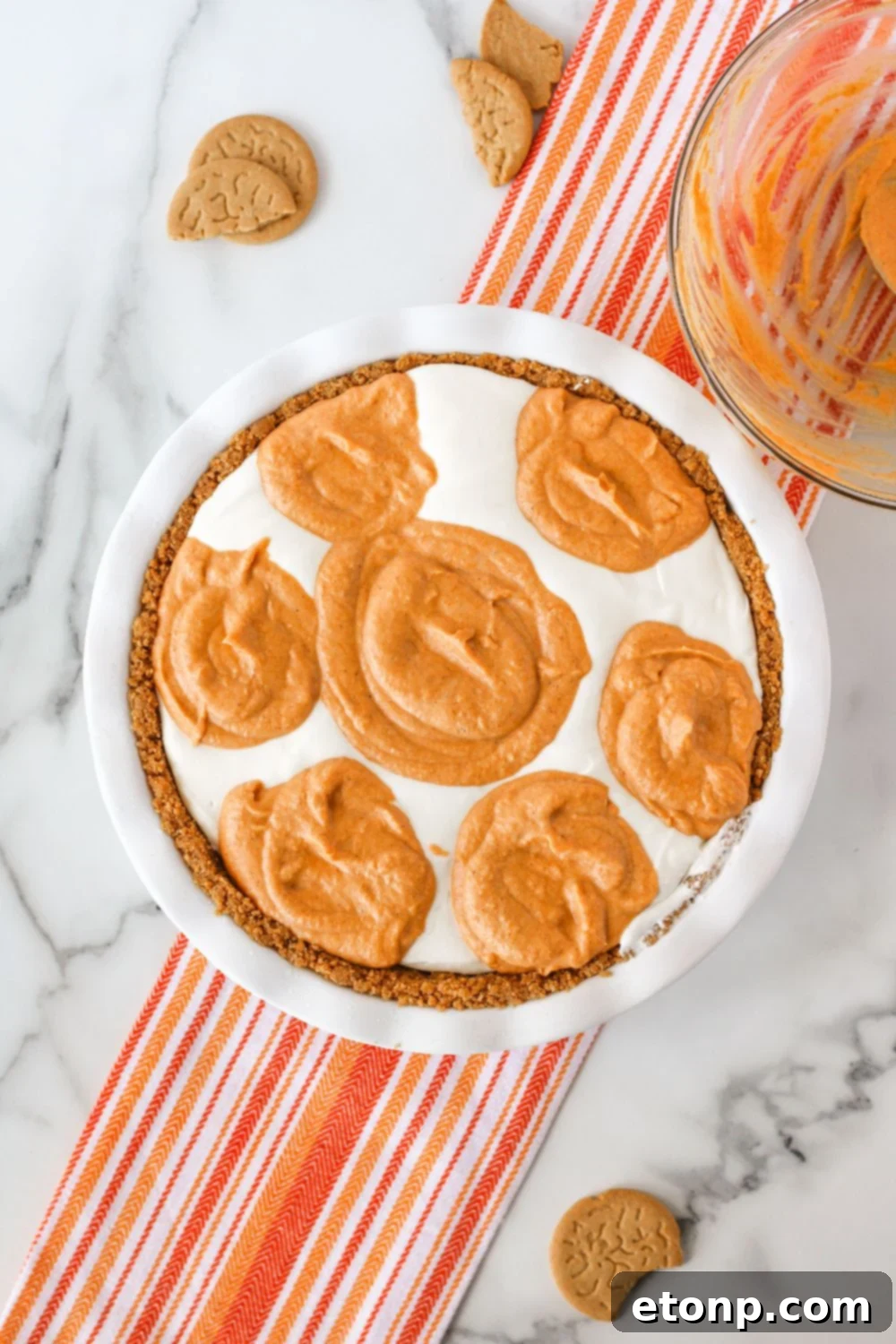 An overhead process image demonstrating how to layer and swirl the pumpkin spice ice cream pie mixture within the crust.