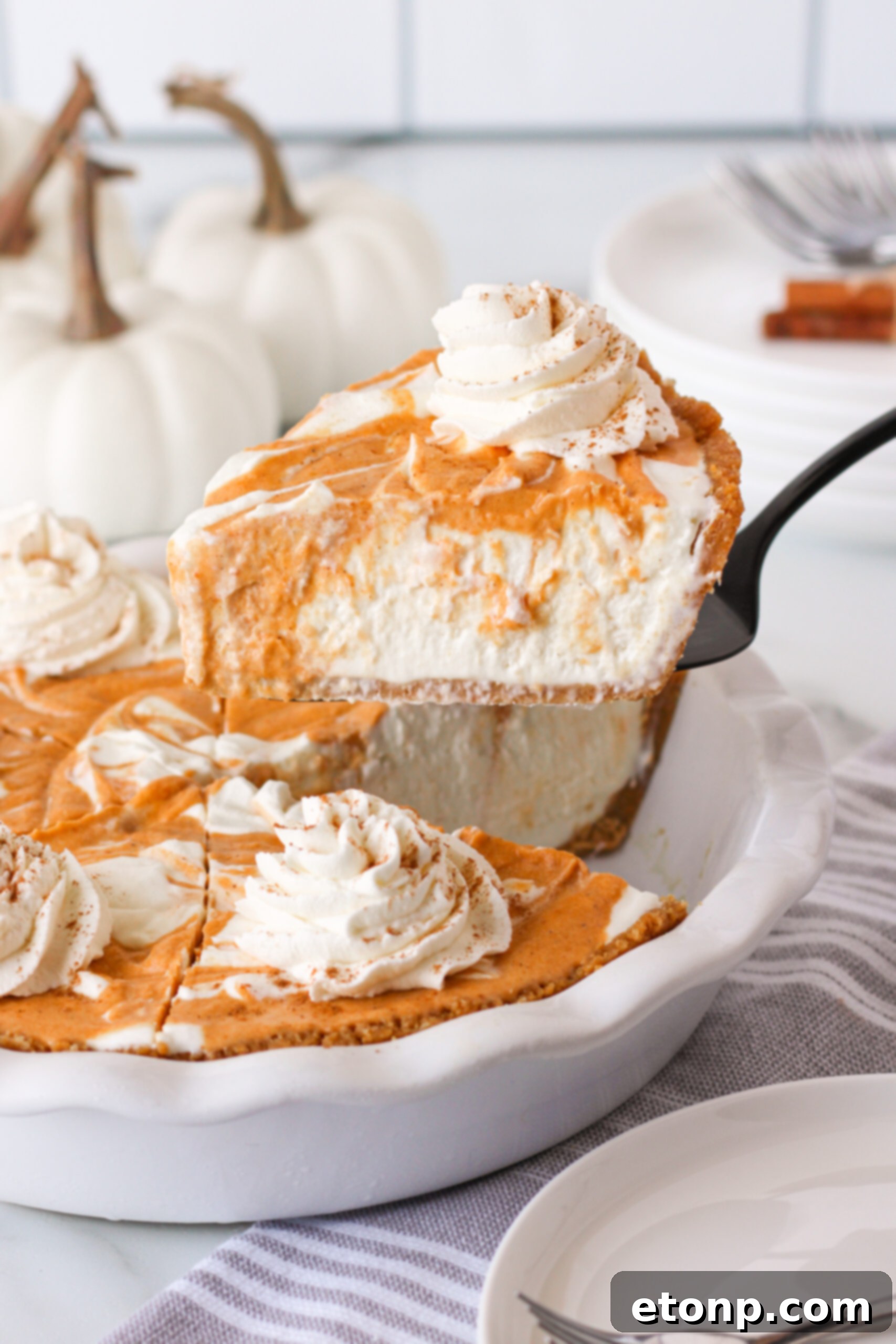 A Pumpkin Ice Cream Pie, with a perfectly cut slice being carefully lifted out of a white baking dish, highlighting its readiness to serve.