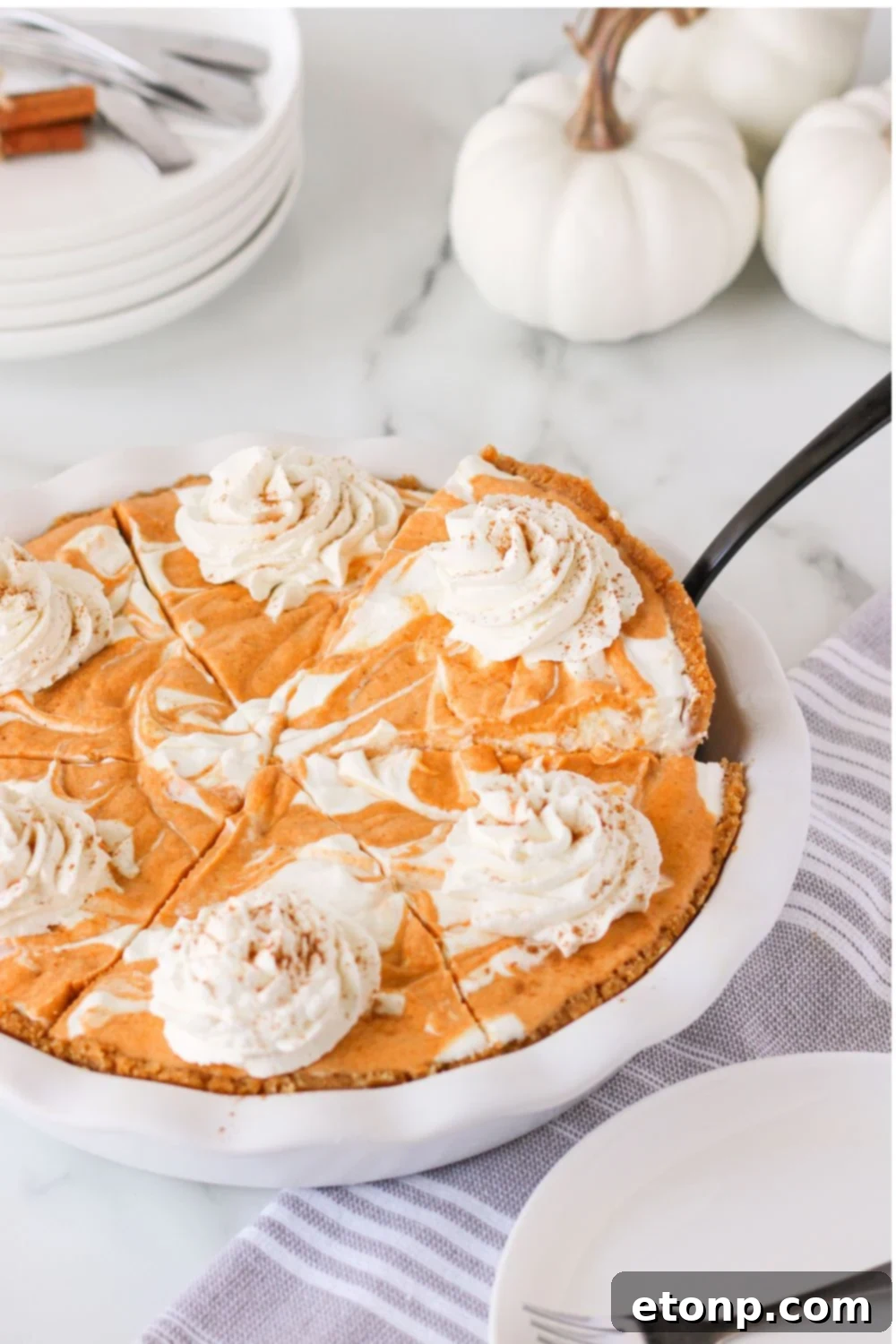 A pumpkin pie ice cream cake presented in a pan, with a spatula poised to lift out a perfect slice, inviting indulgence.
