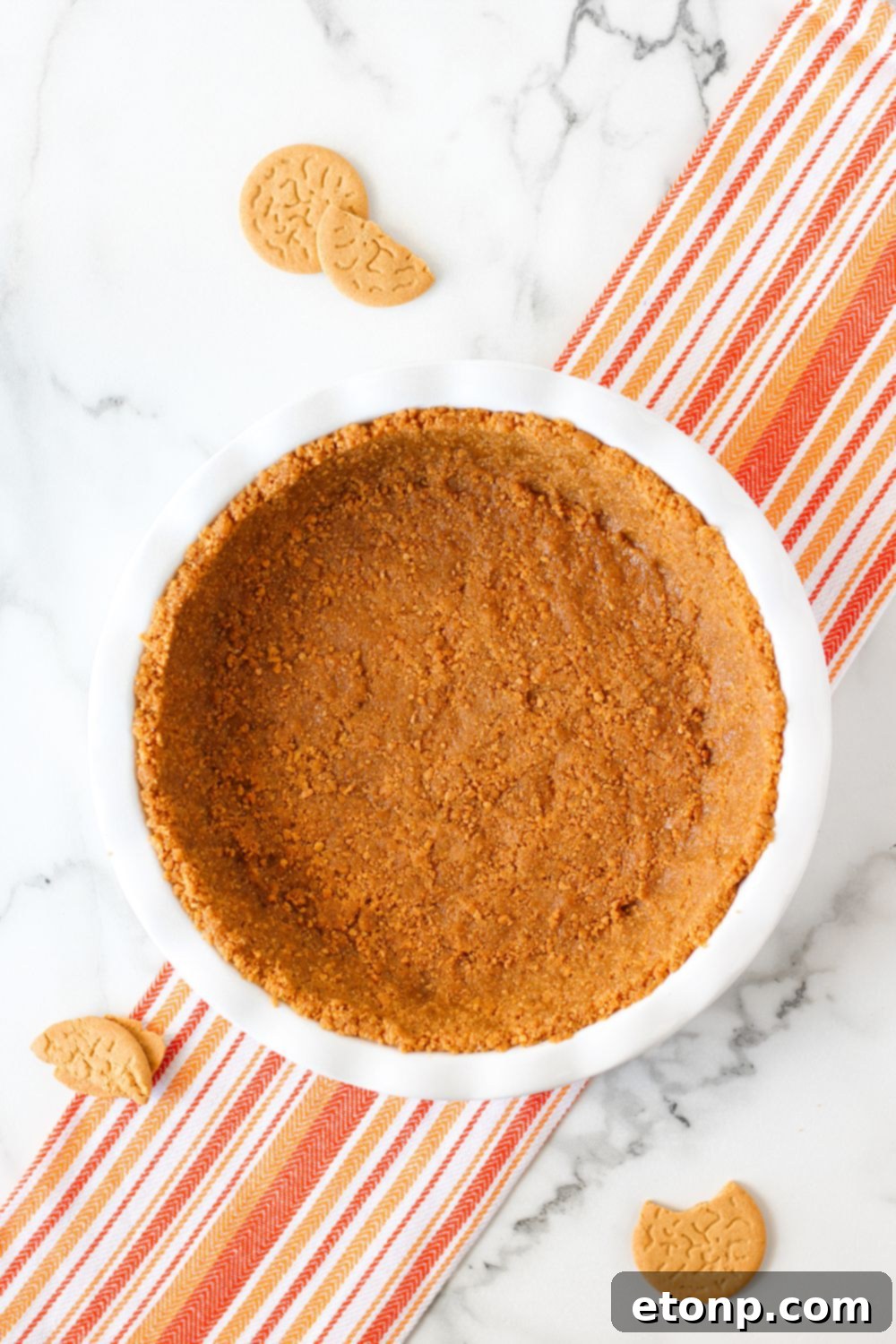 The golden-brown gingersnap crust, meticulously formed in a pie pan and resting on a table, illustrating the perfect base for the pie.