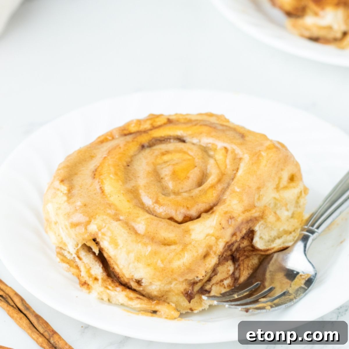 A single pumpkin cinnamon roll on a plate with a fork, showing its rich frosting and swirl