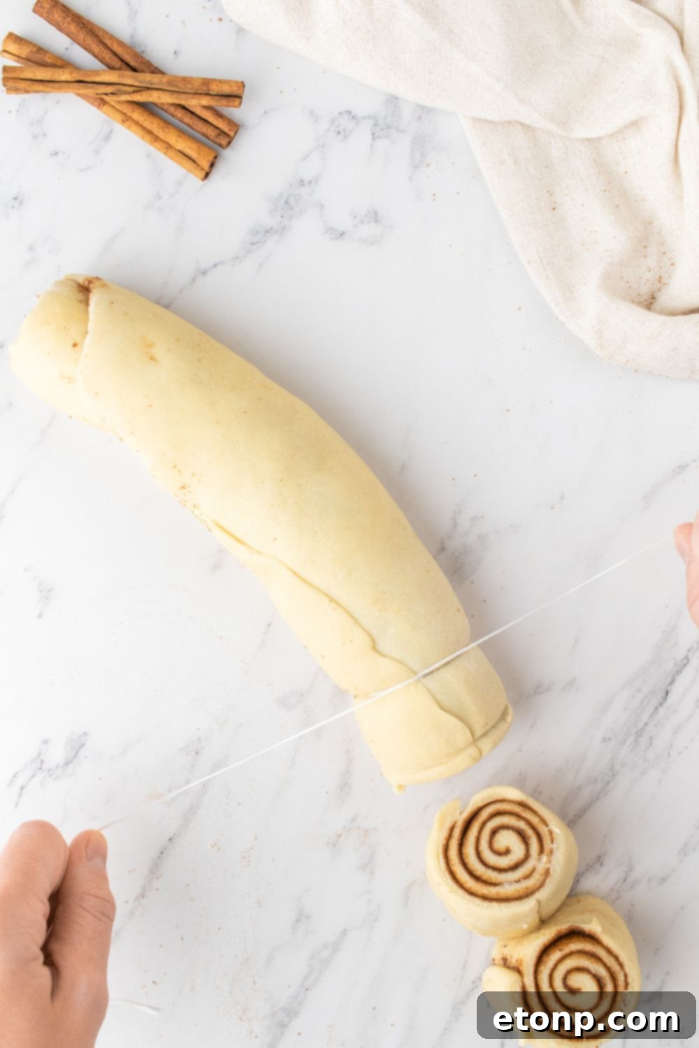 Slicing a rolled cinnamon roll log into individual rolls on a marble counter