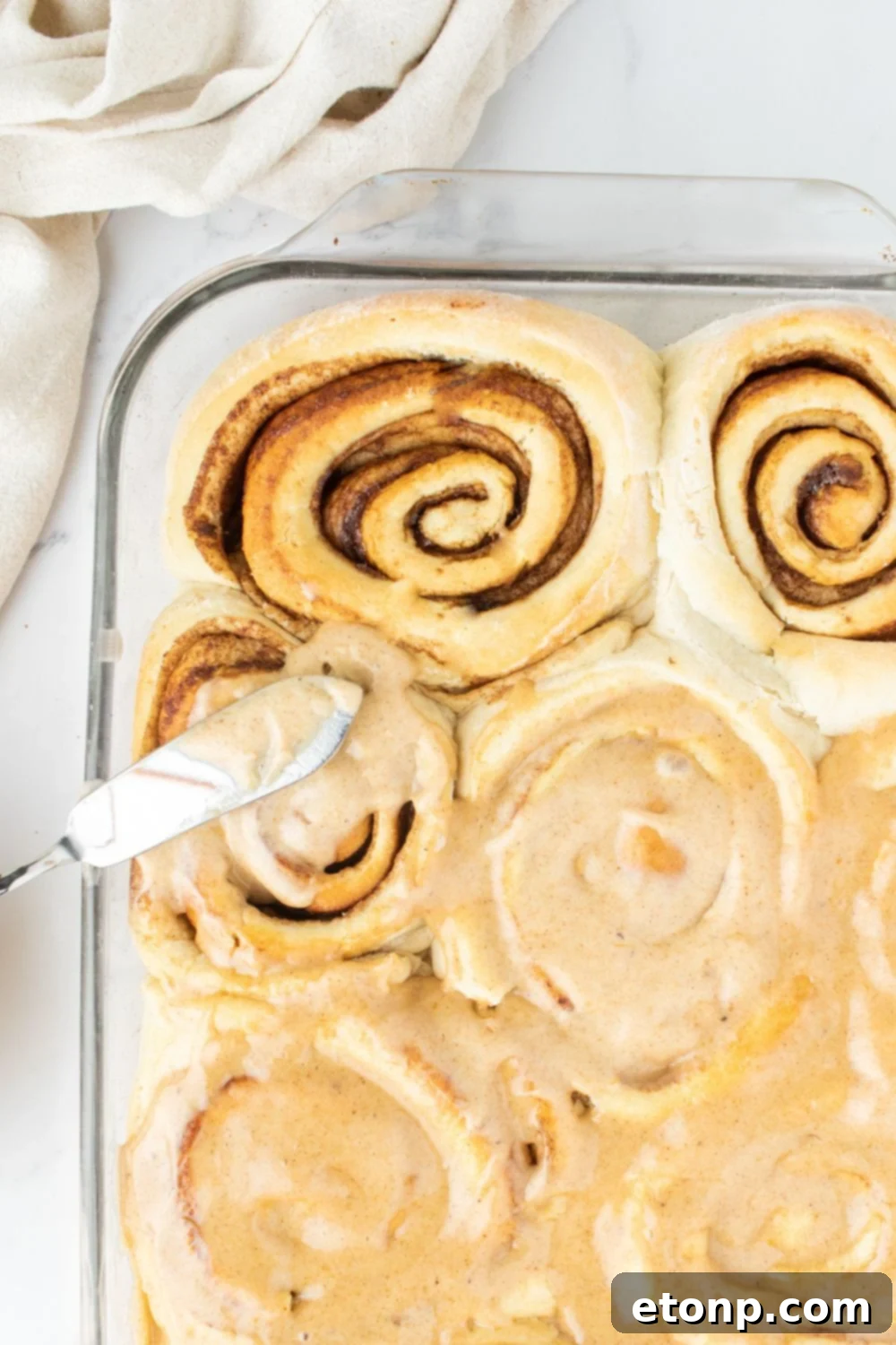 Spreading creamy pumpkin spice frosting generously over warm cinnamon rolls in a pan