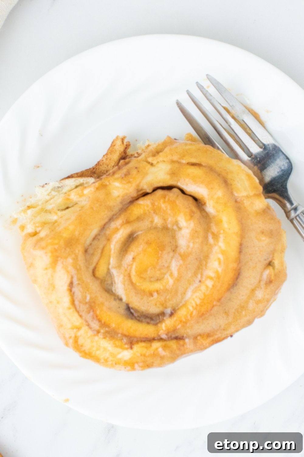 Overhead shot of a single pumpkin cinnamon roll on a plate, showcasing its fluffy texture and generous frosting