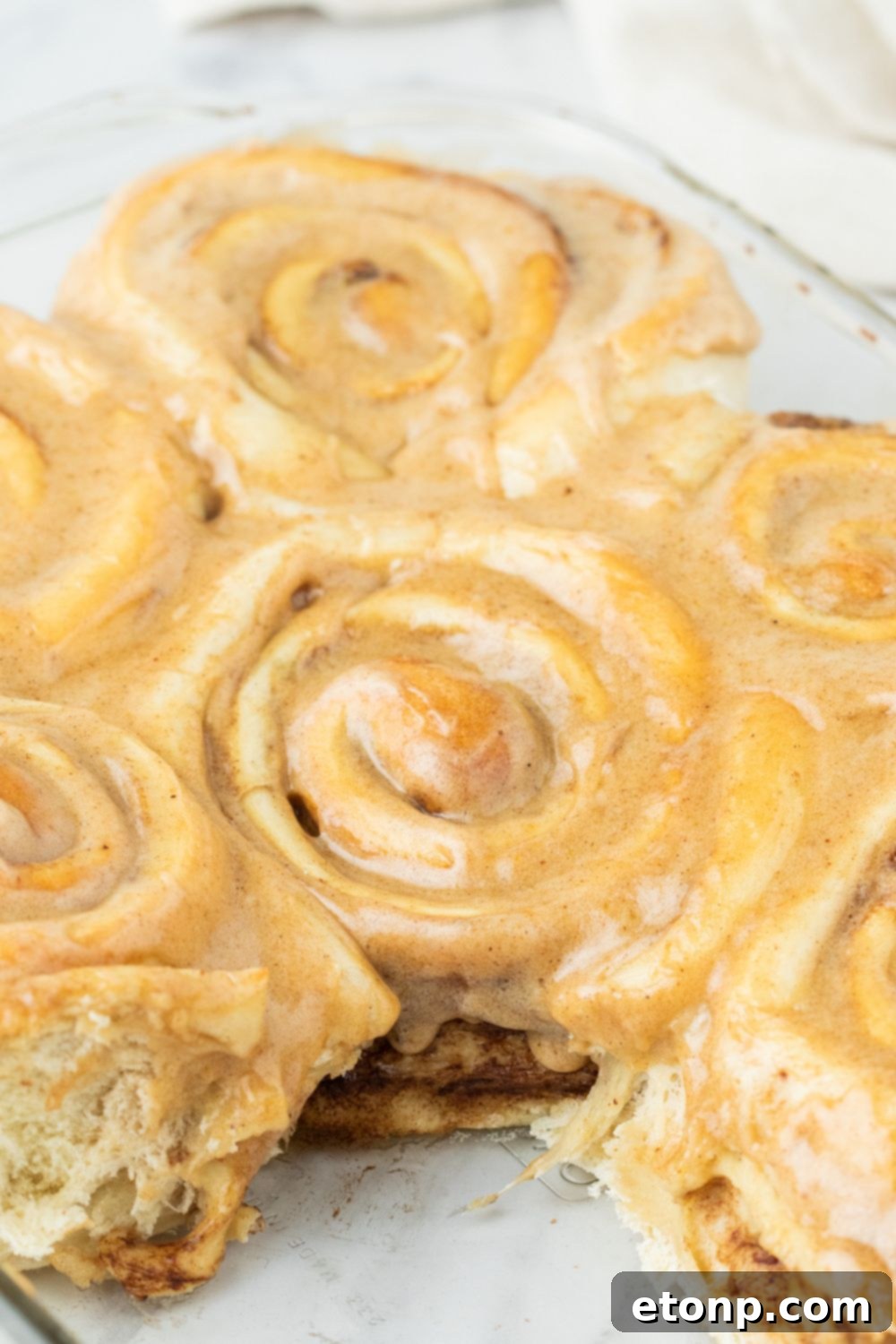 A baking pan of pumpkin cinnamon rolls with one roll removed, showing the golden-brown edges
