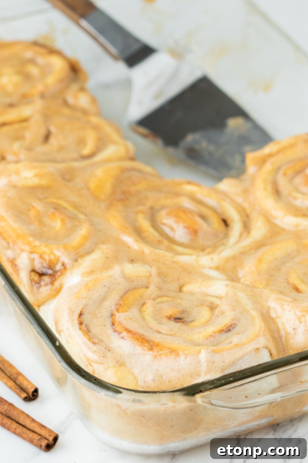 A close-up of baked pumpkin cinnamon rolls in a pan, with some frosting already spread
