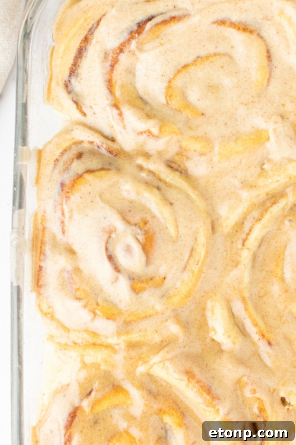 A pan full of pumpkin spice cinnamon rolls, freshly baked and lightly frosted