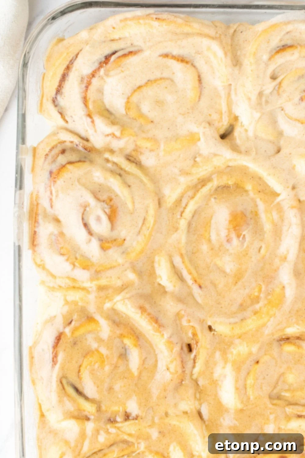 Overhead shot of freshly baked pumpkin cinnamon rolls in a glass baking pan on a rustic table