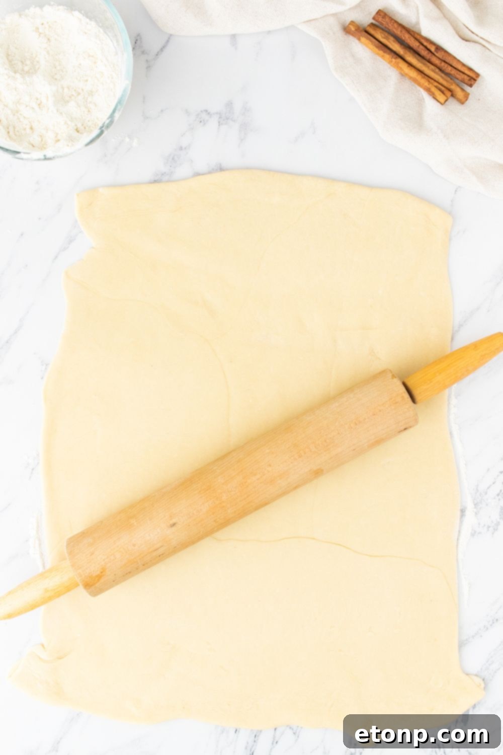A person rolling out dough on a floured surface with a rolling pin