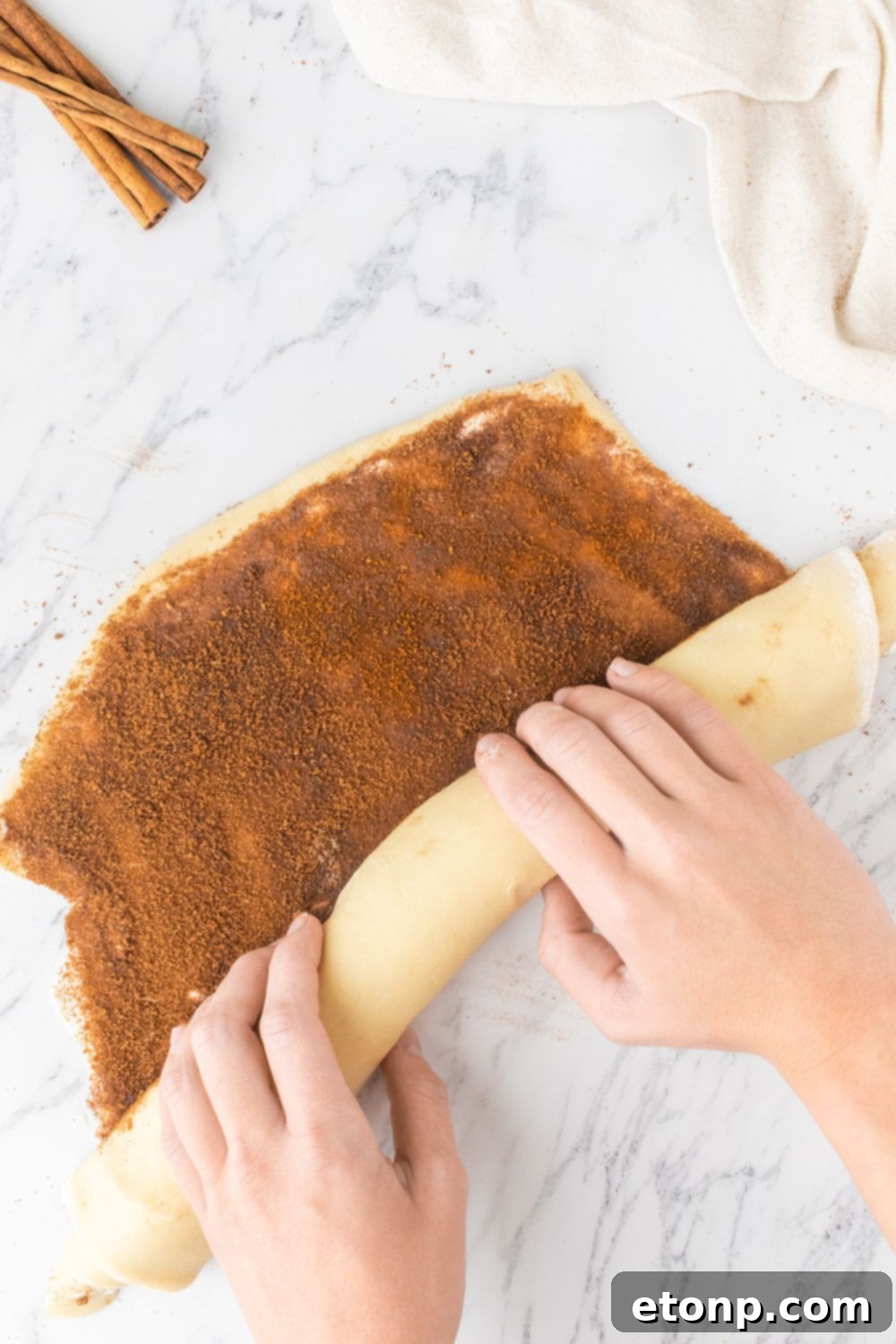 Rolling cinnamon roll dough into a tight tube after adding filling