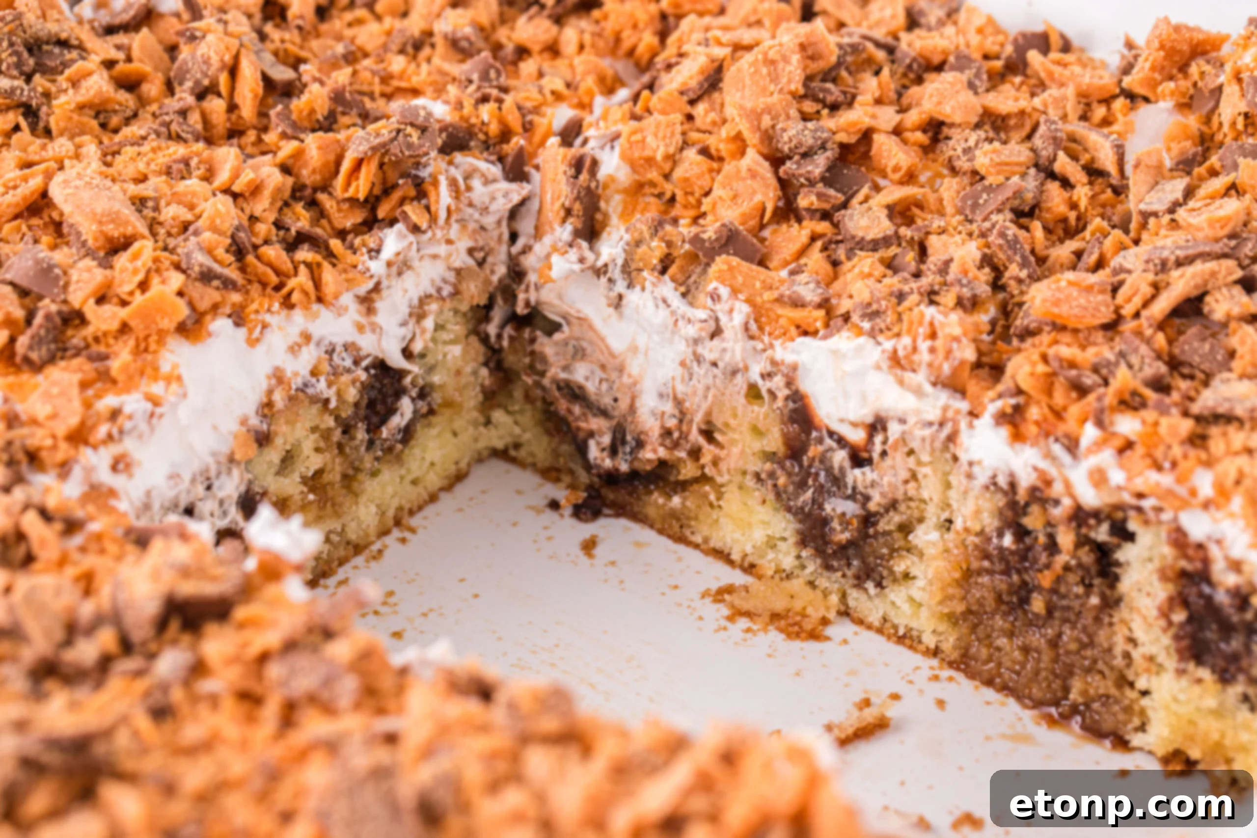 Butterfinger Poke Cake in a white baking dish with a couple slices removed