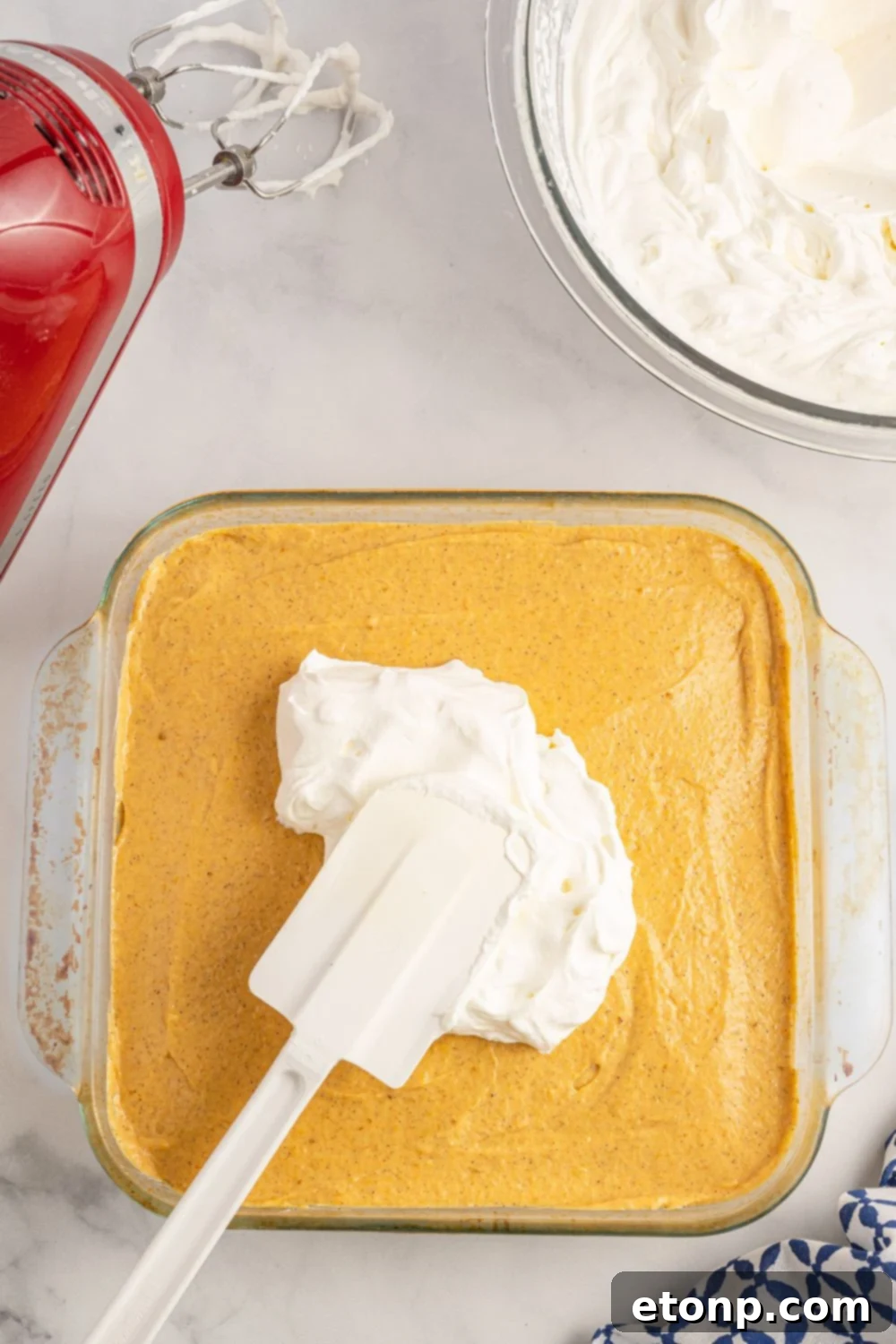 spreading whipped cream over the top of a pumpkin layered dessert 