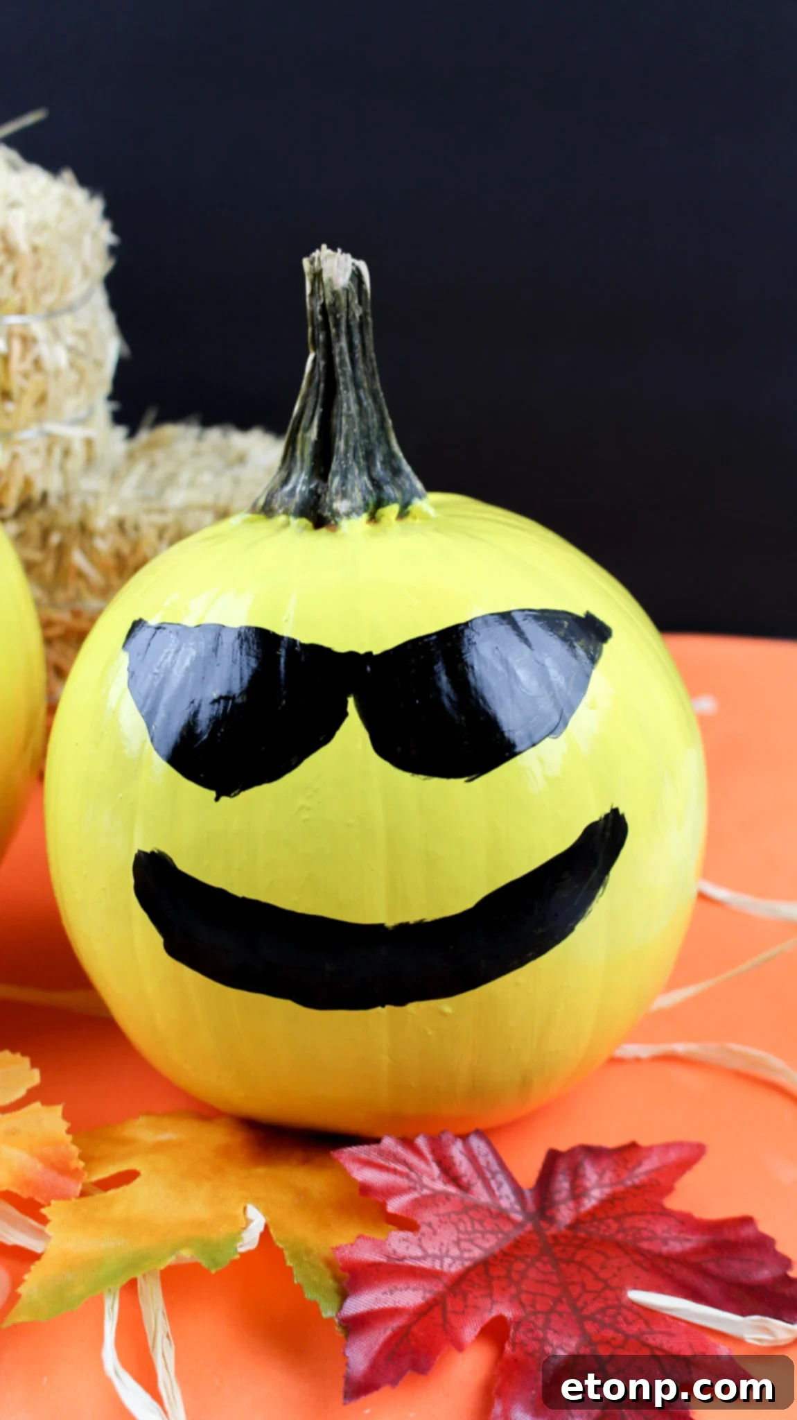 A vibrant yellow pumpkin painted with the 'cool' emoji face, complete with black sunglasses and a confident smile.