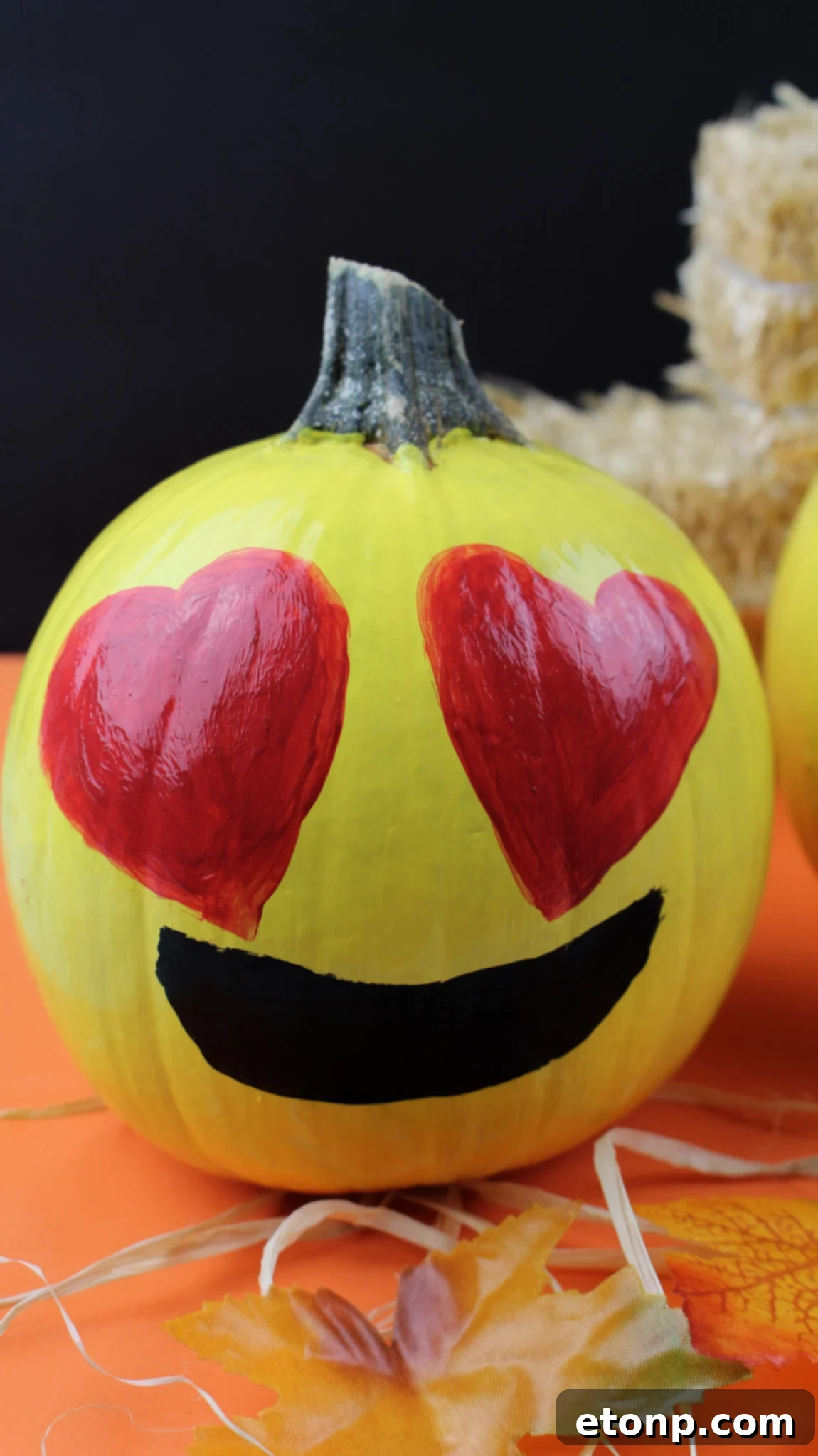 A yellow painted pumpkin featuring a winking emoji face with a silly tongue sticking out, adorned with a black outline and pink tongue.