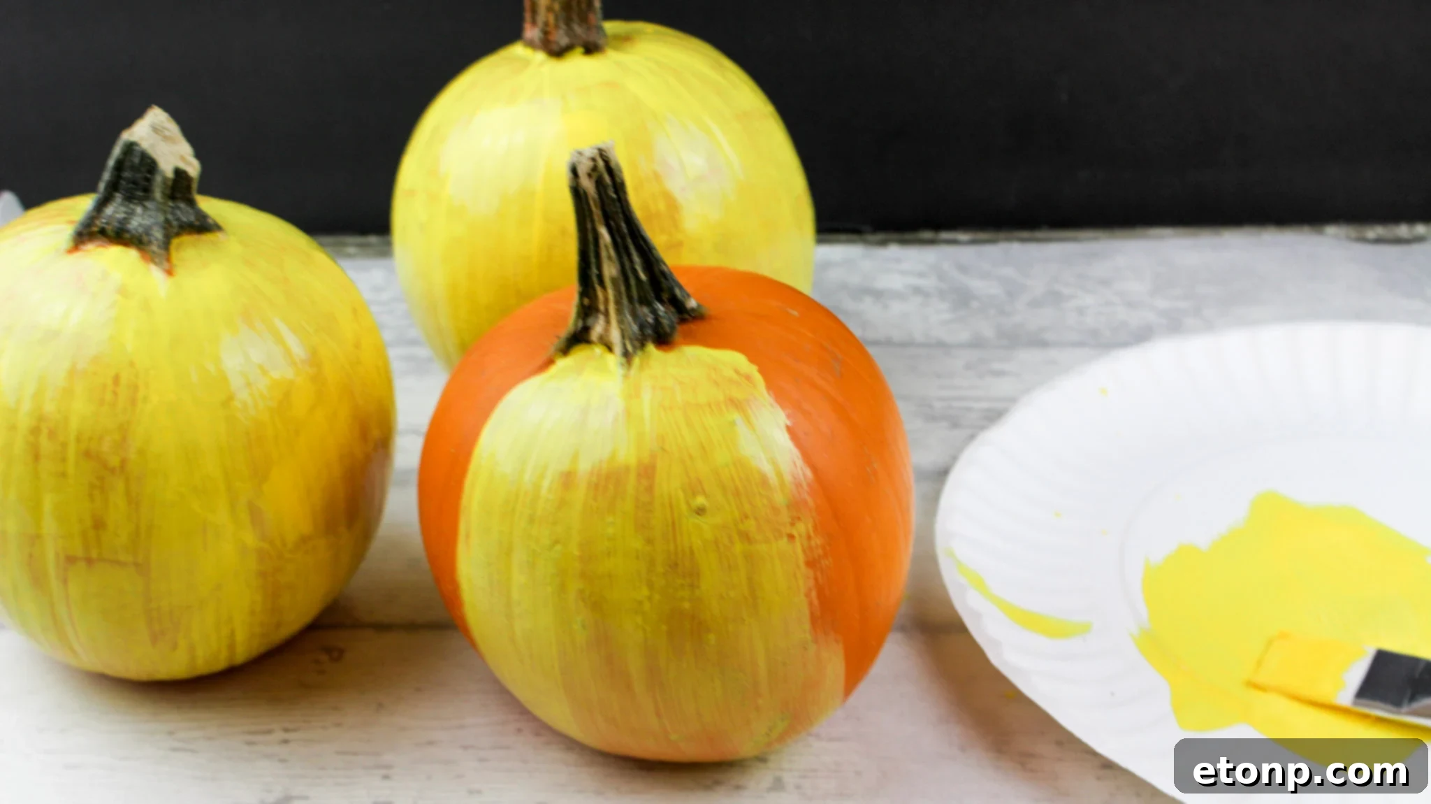 Two yellow painted pumpkins with emoji faces, one with heart eyes and a smile, the other with a winking eye and a silly tongue sticking out.