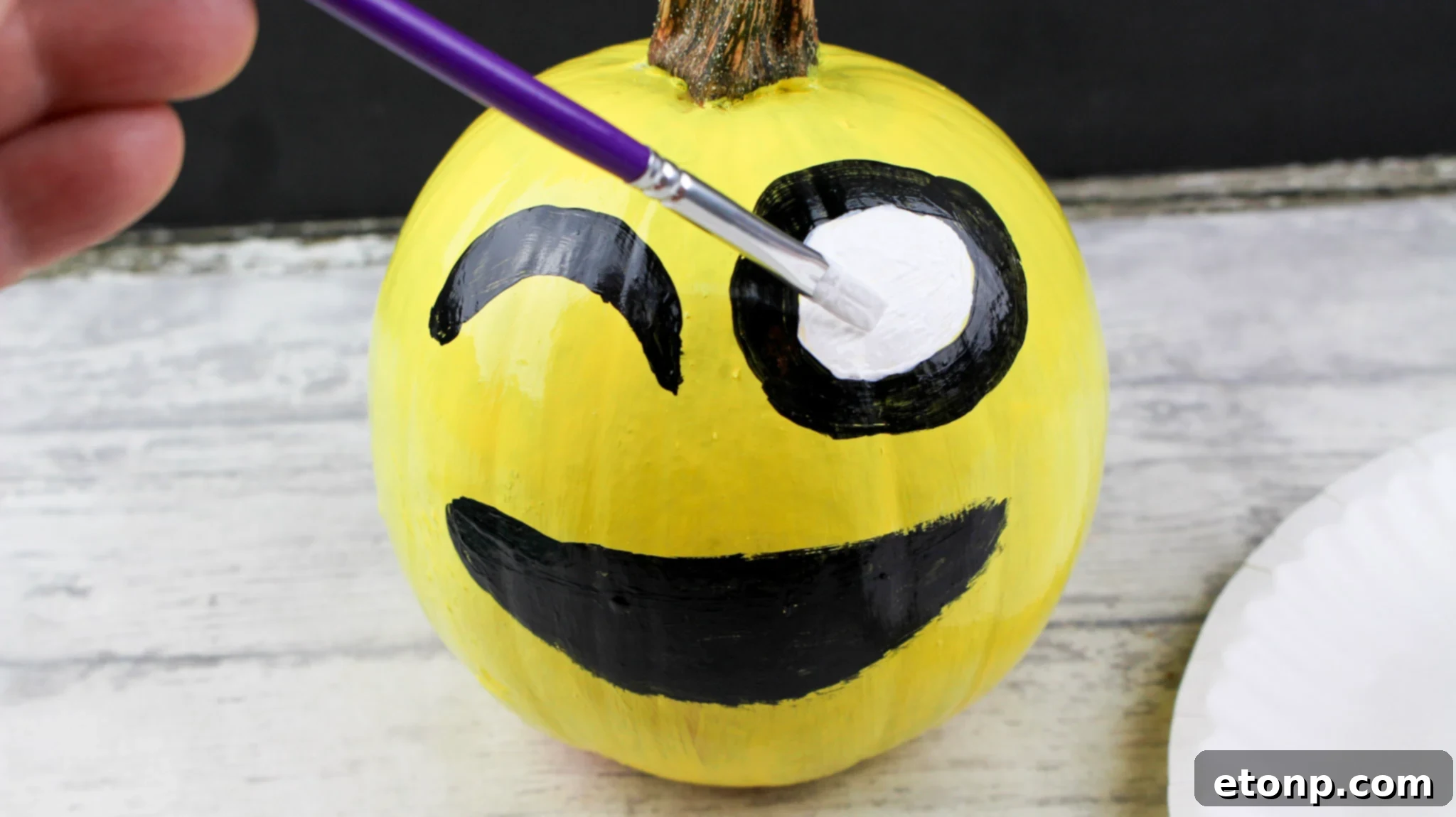 Close-up of a yellow painted pumpkin with a heart-eye emoji face, showing intricate details of the red hearts and black smile.