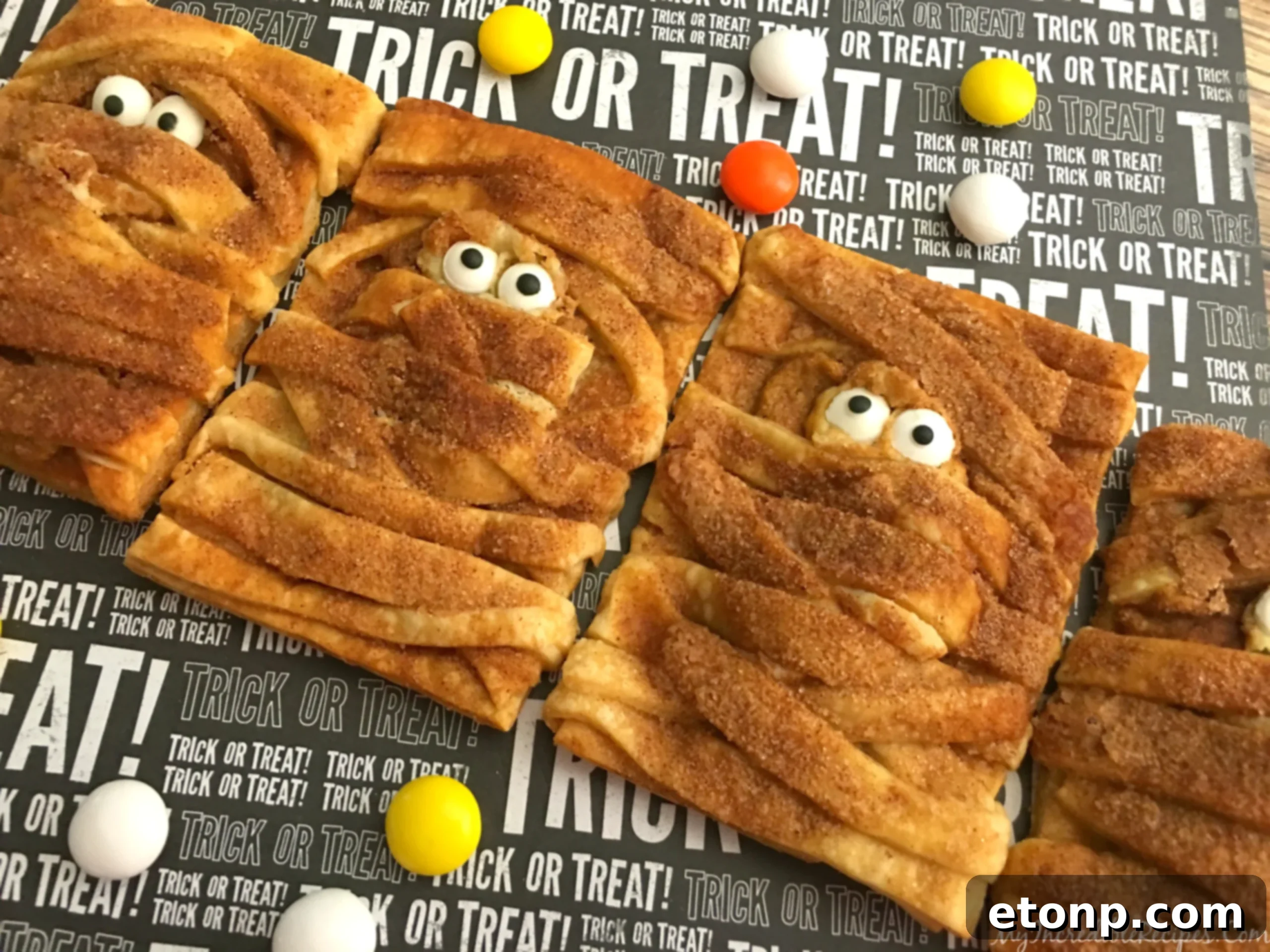 Final assembly of ultra-cute pumpkin cheesecake mummy hand pies with candy eyes after baking.