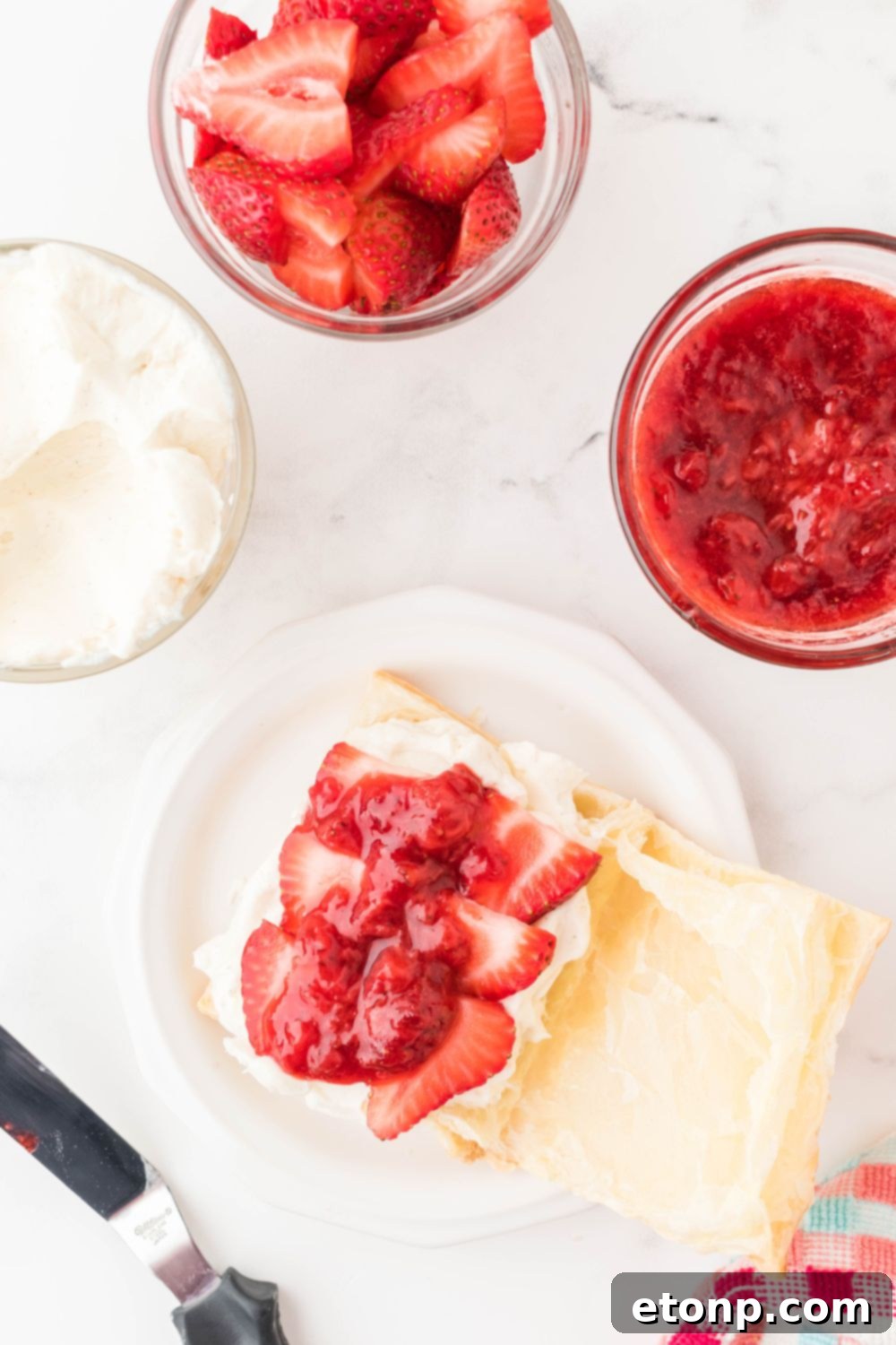 An opened puff pastry generously filled with creamy cream cheese mixture and layered with fresh strawberry slices, ready for the compote.