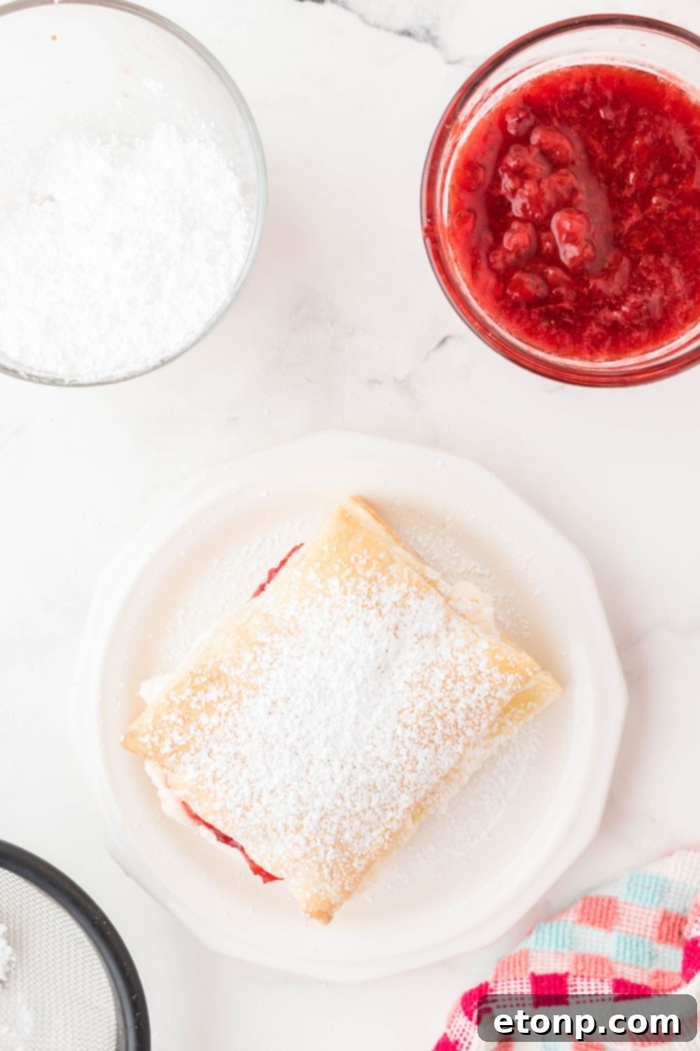 A finished Strawberry Flaky Puff, elegantly dusted with powdered sugar, presented on a plate and ready to be enjoyed.