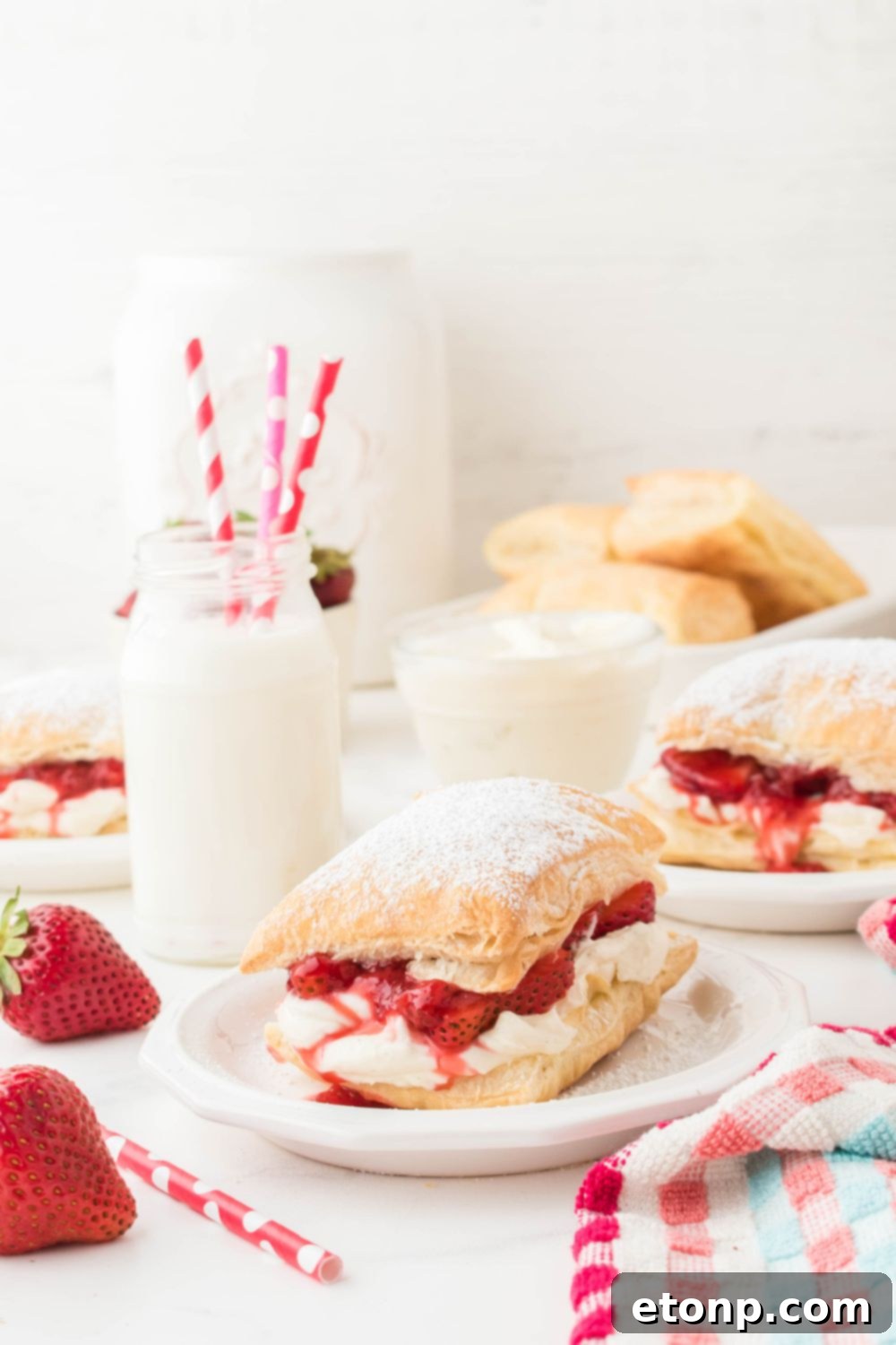 Strawberry shortcake puffs artfully arranged on plates, accompanied by charming jars of milk with paper straws, creating a rustic and inviting dessert setting.